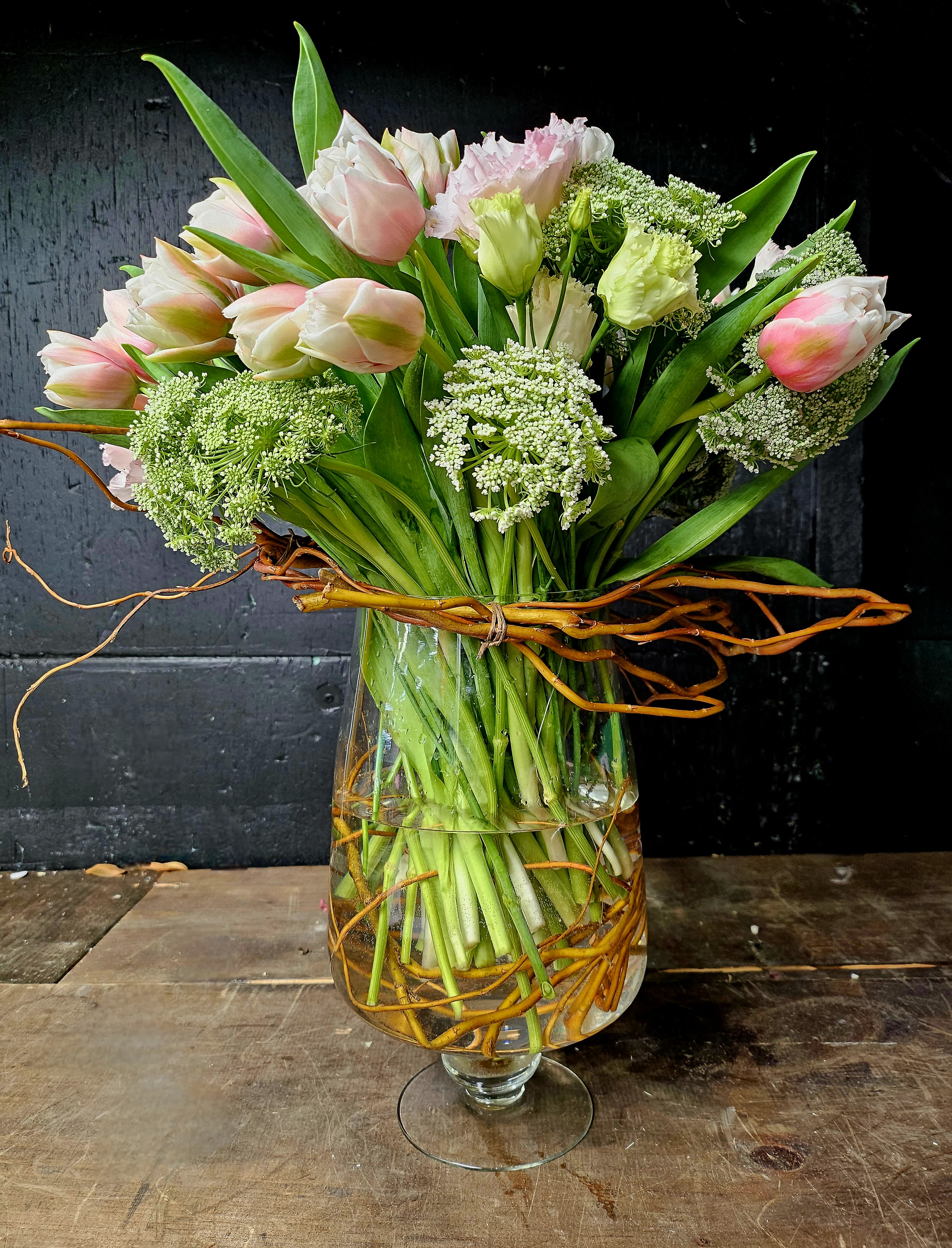 Pink and white tulips arranged in a glass vase with curly branches
