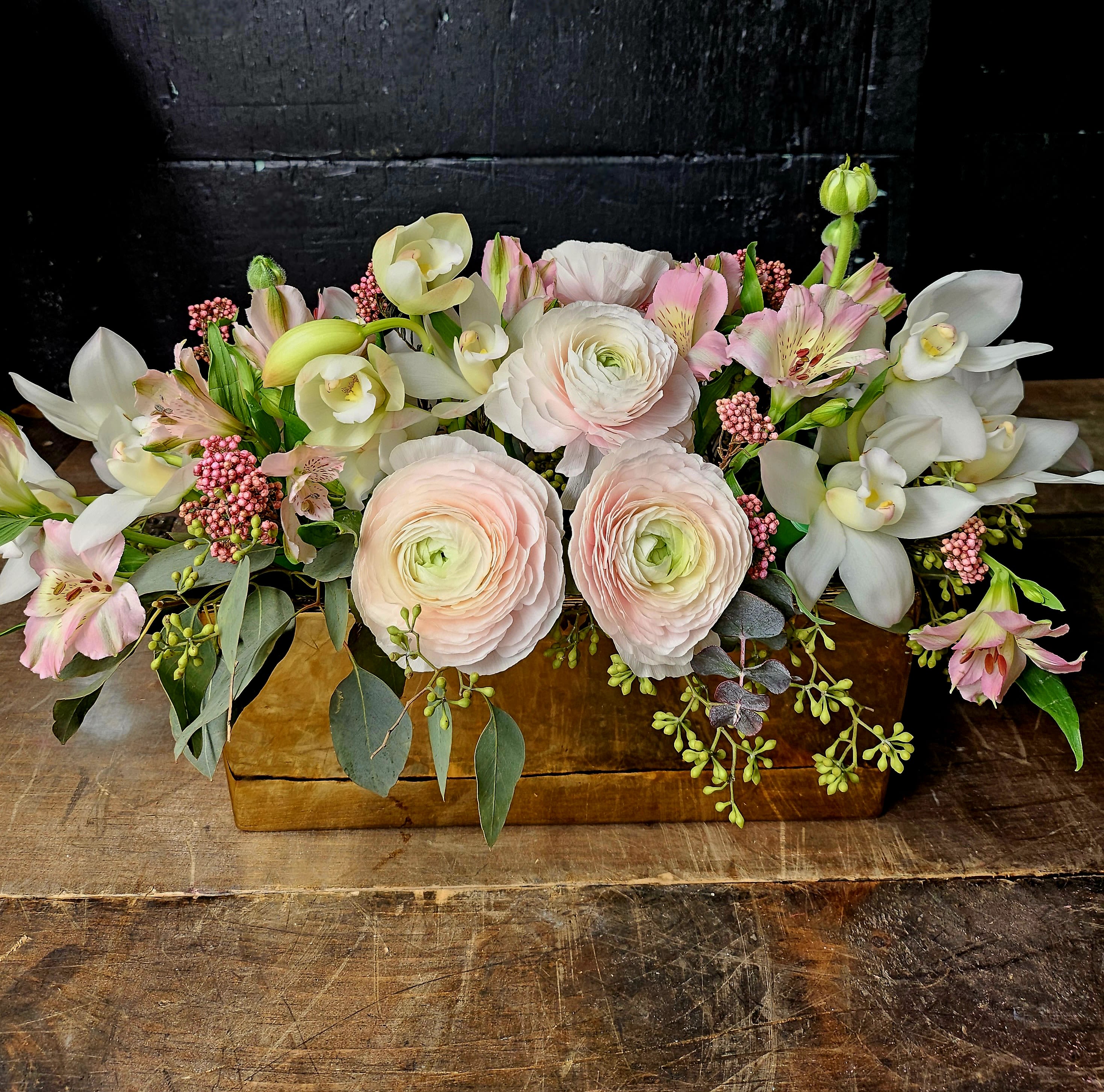 Low floral arrangement with pale pink ranunculus and white orchids in a wooden box