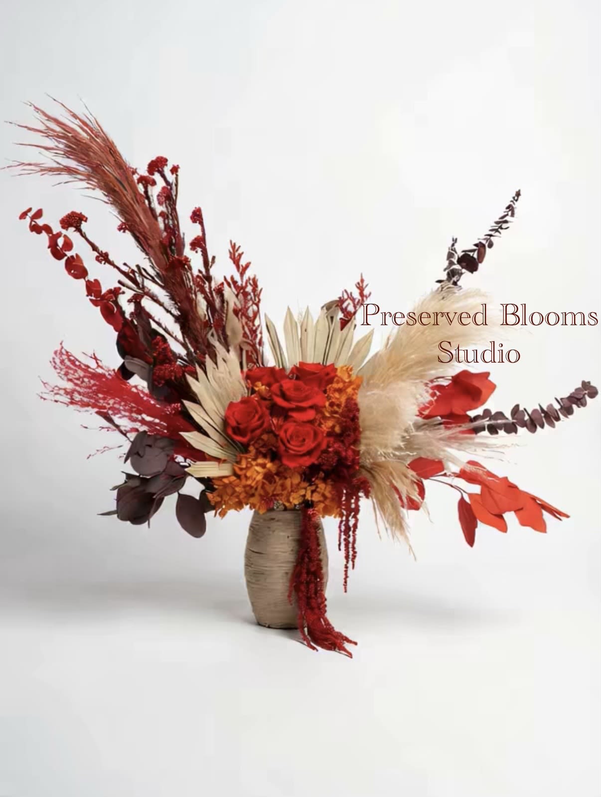 Tall asymmetrical arrangement of red roses and dried botanicals in a neutral ceramic vase