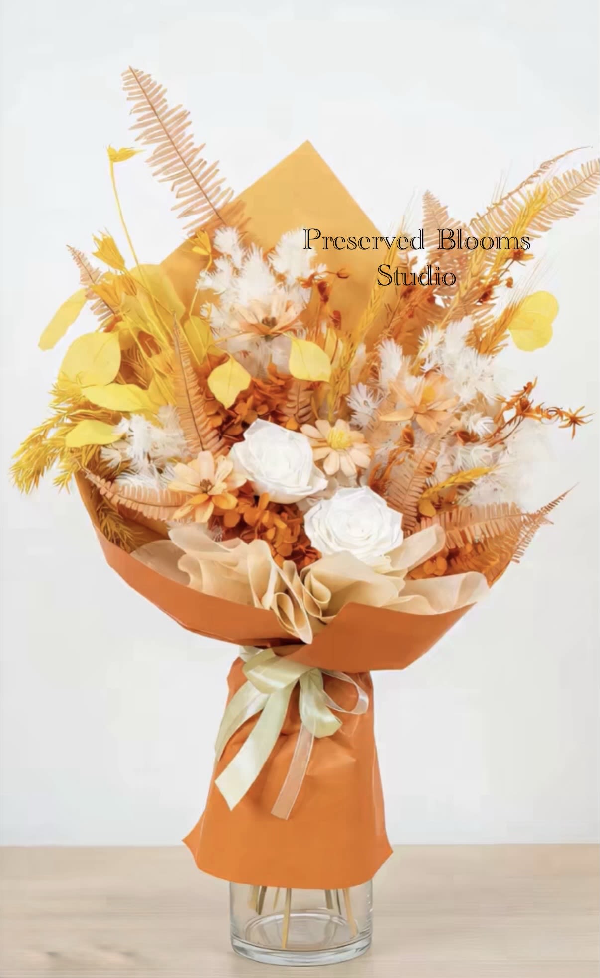 Tall bouquet of orange and yellow dried flowers with white roses wrapped in orange paper with ribbon