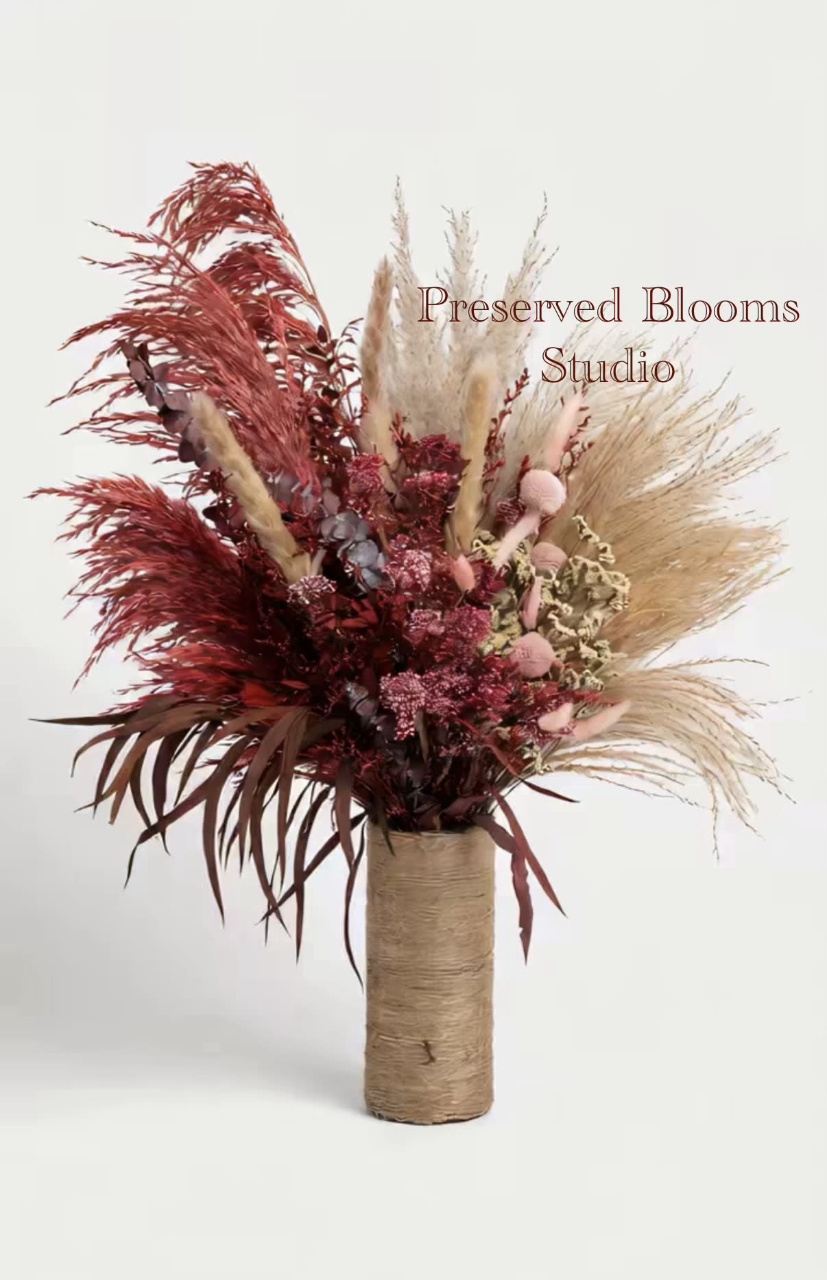 Tall dried arrangement of red and natural pampas in a twine-wrapped cylinder vase