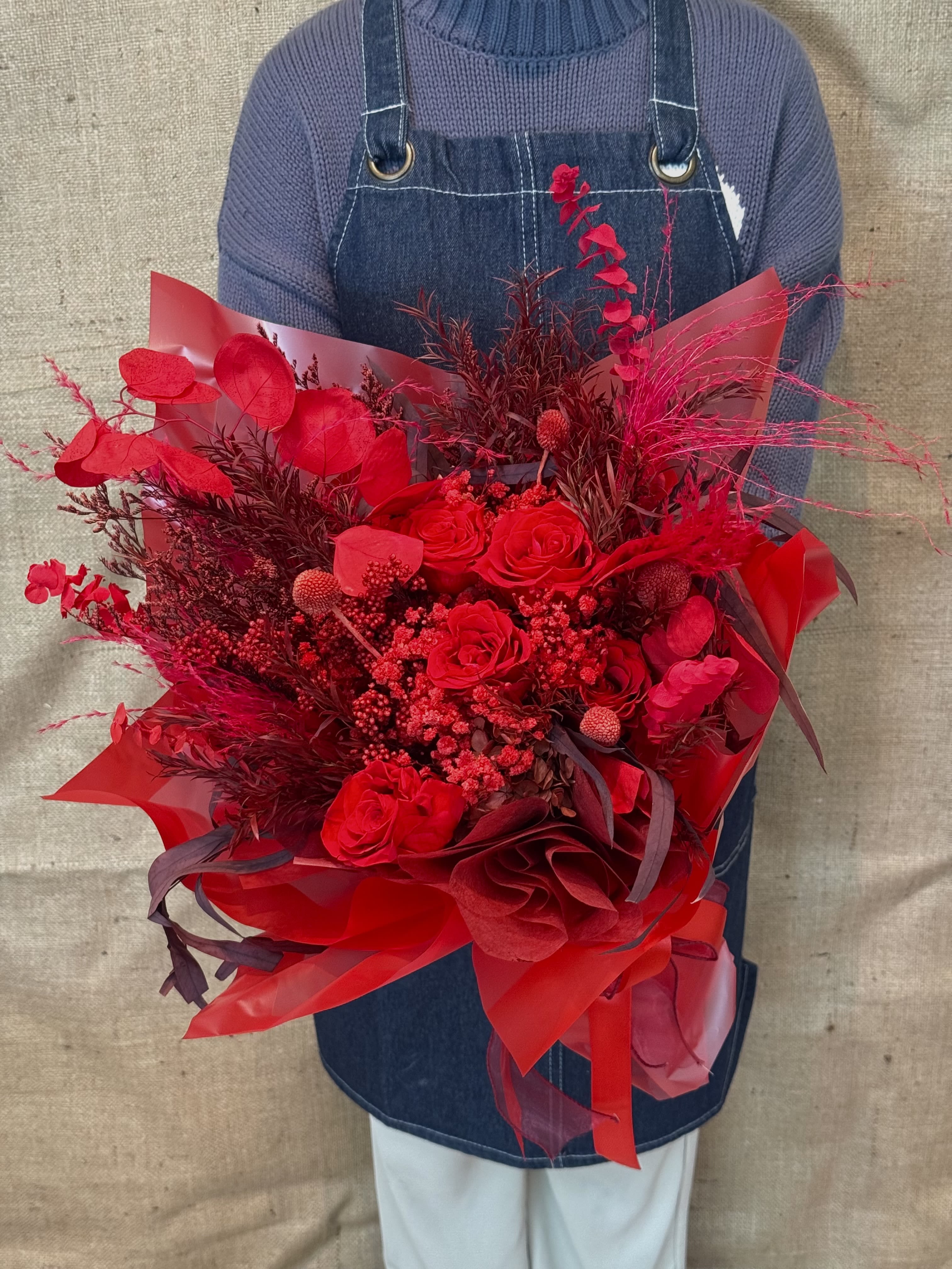 Large red bouquet of roses and decorative foliage wrapped in red paper