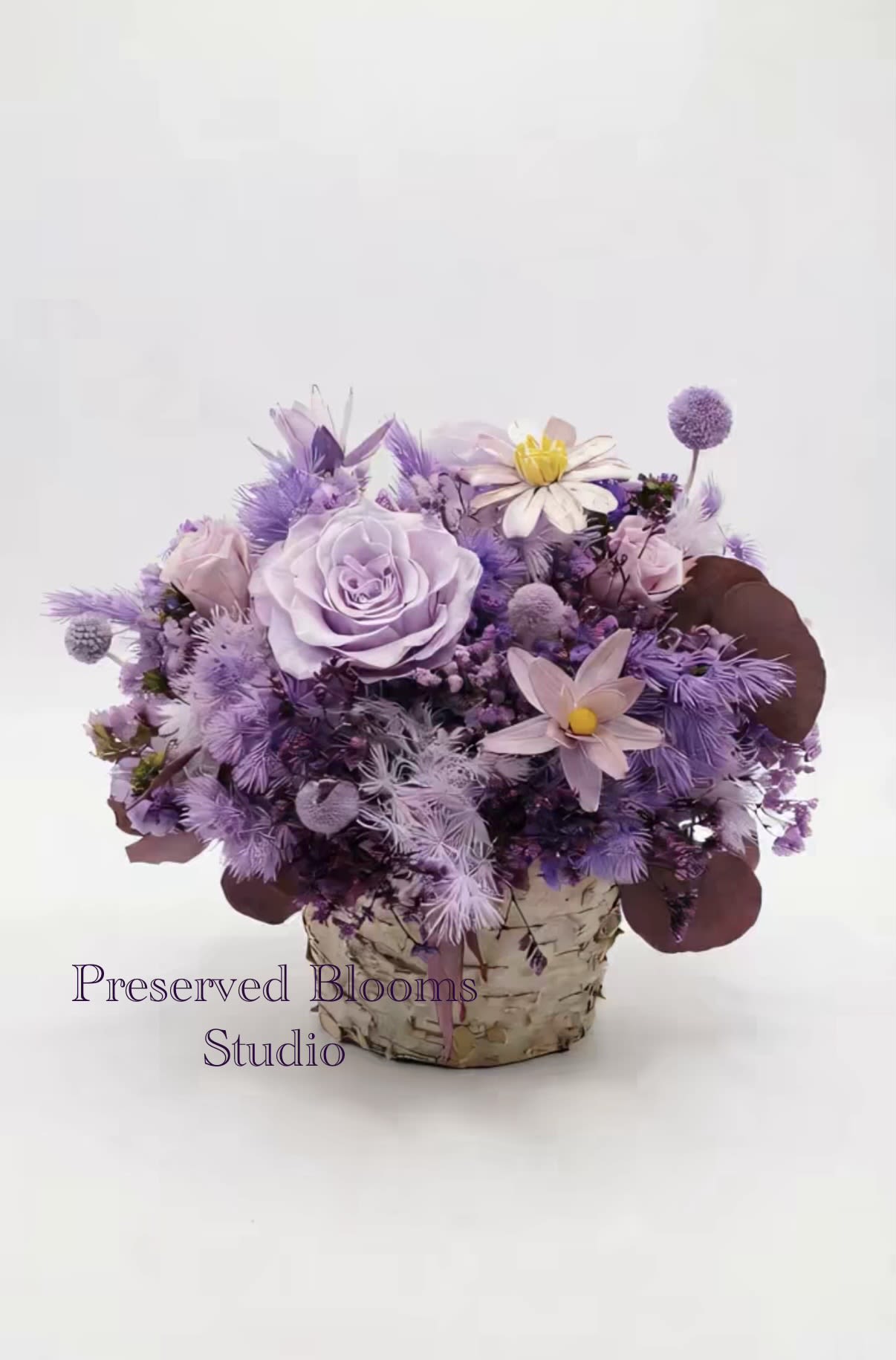 Lavender and purple flower arrangement with roses and daisies in a birch-wrapped pot