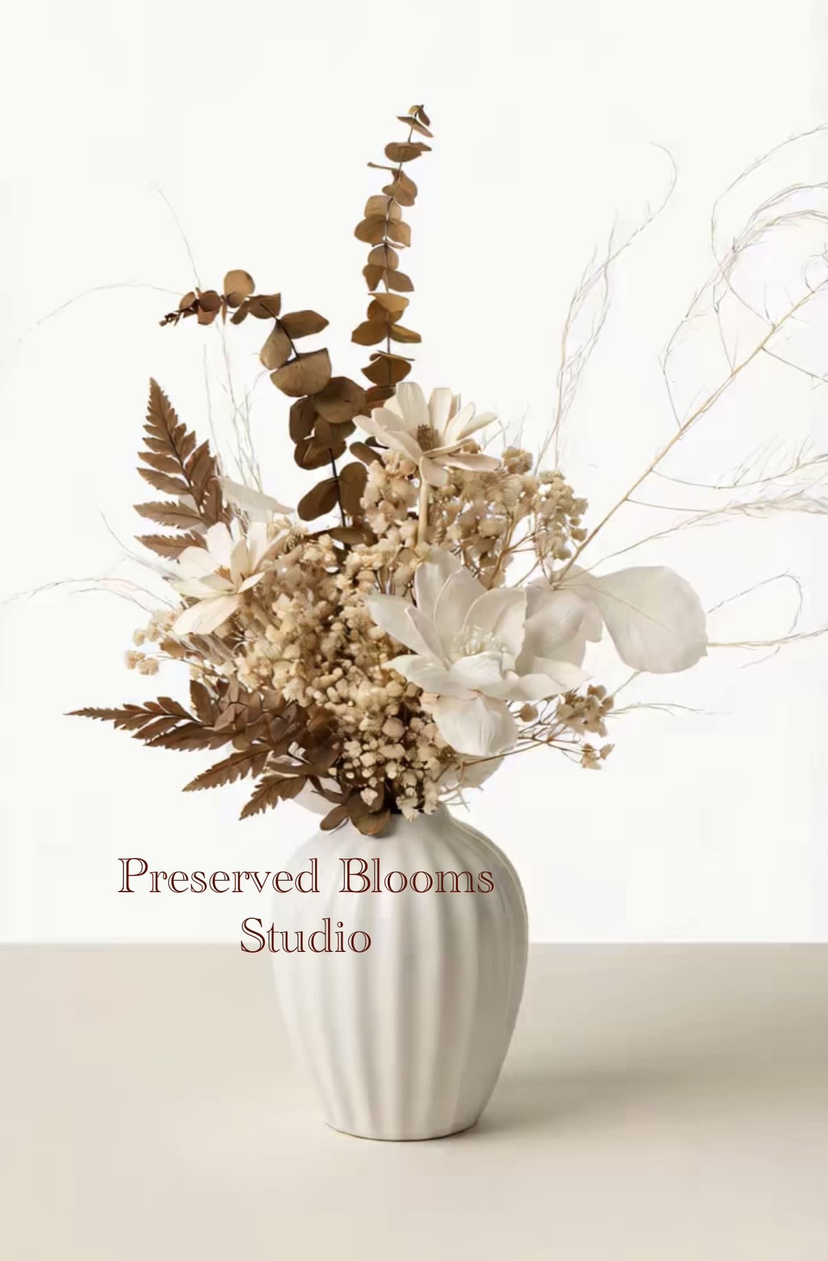 Neutral dried flower arrangement with white blooms and brown foliage in a white ceramic vase