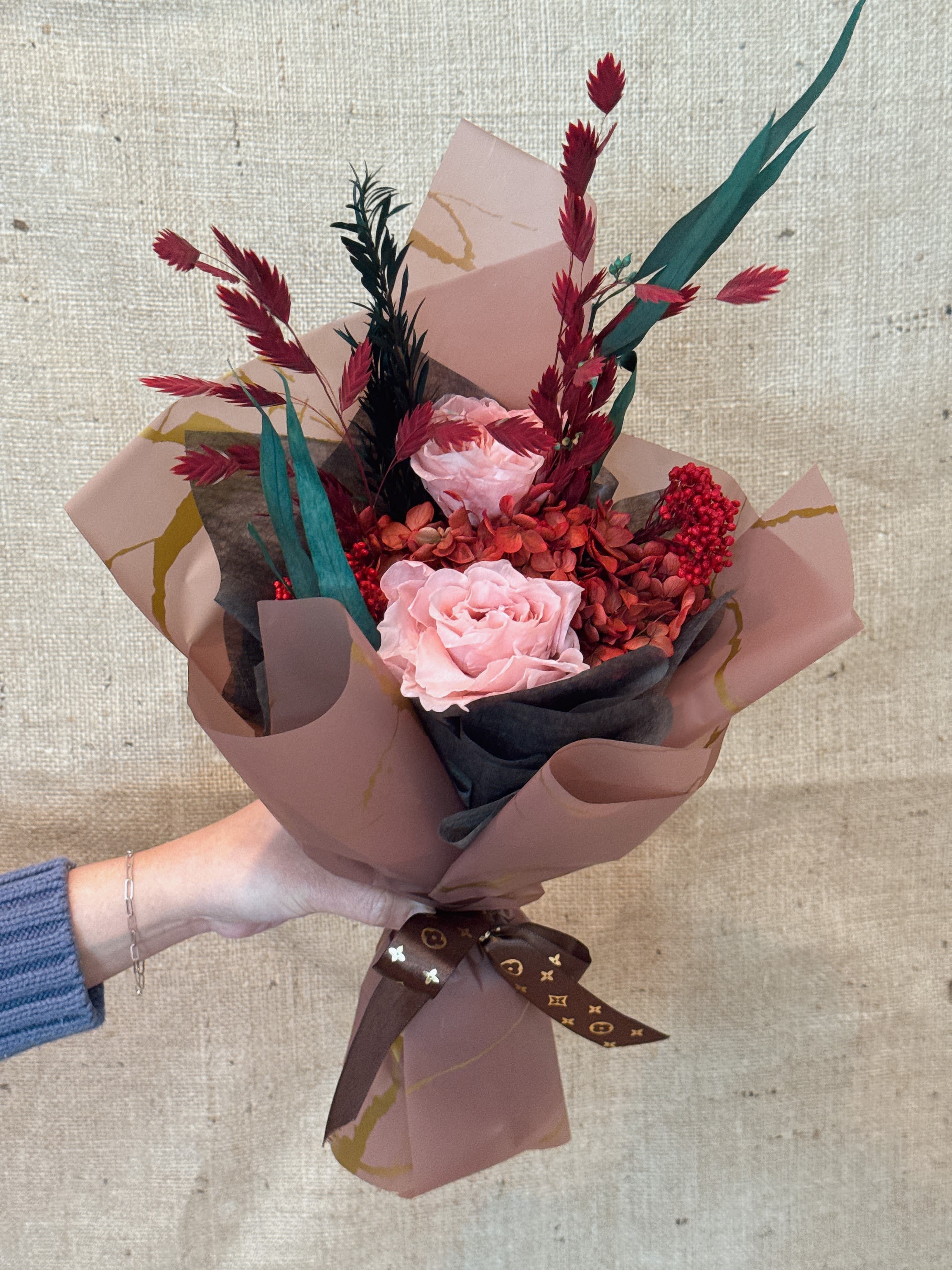 Handheld bouquet of pink roses with red accents and decorative wrap