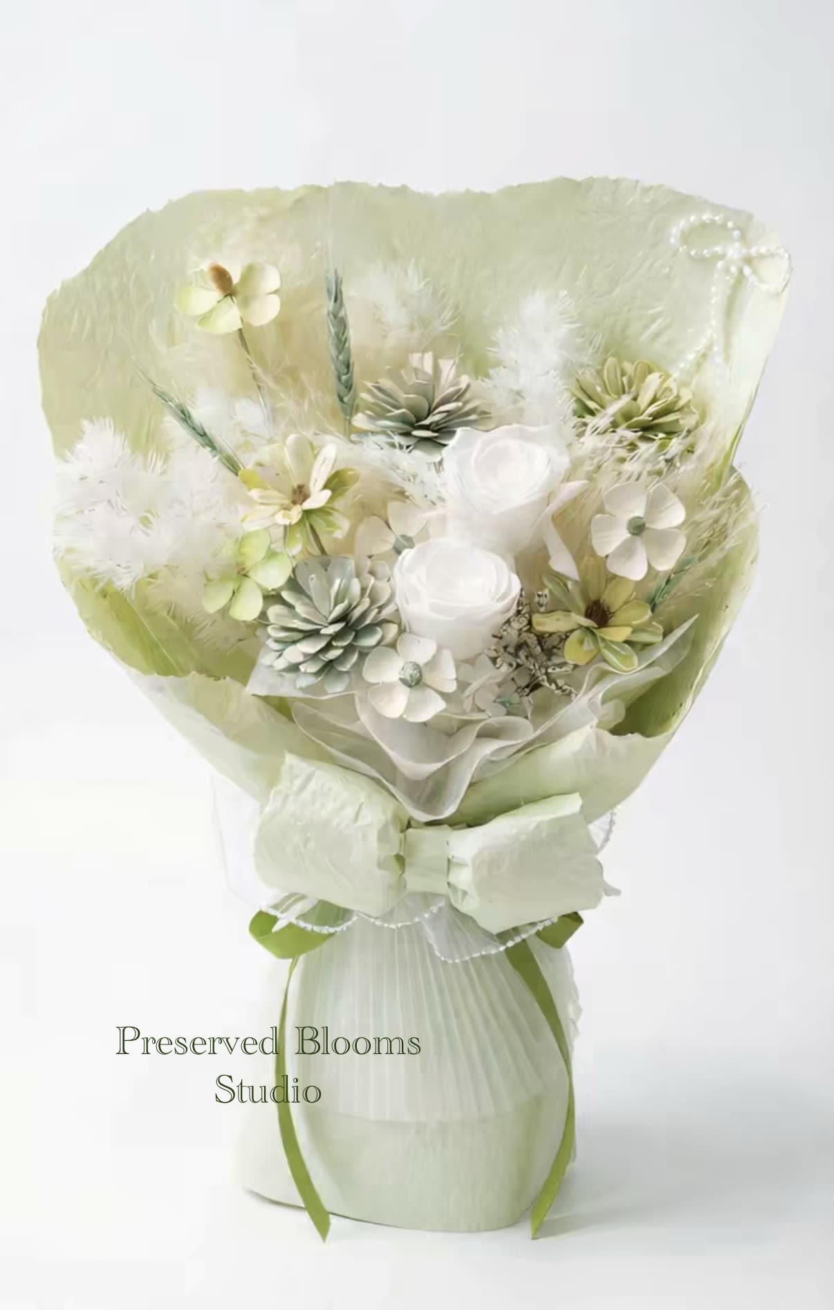 Pale green and white preserved bouquet with roses, small blossoms, and feathers wrapped in matching paper and bow