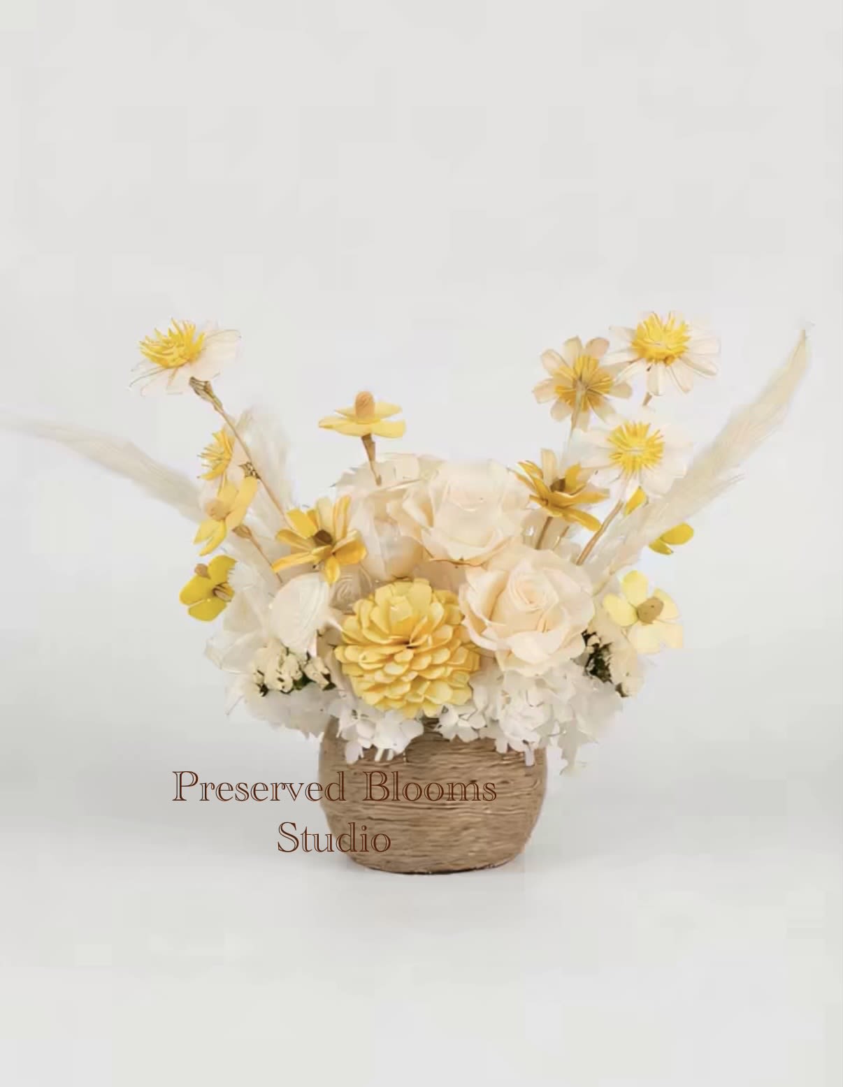 Yellow and cream preserved flower arrangement in a small woven basket container