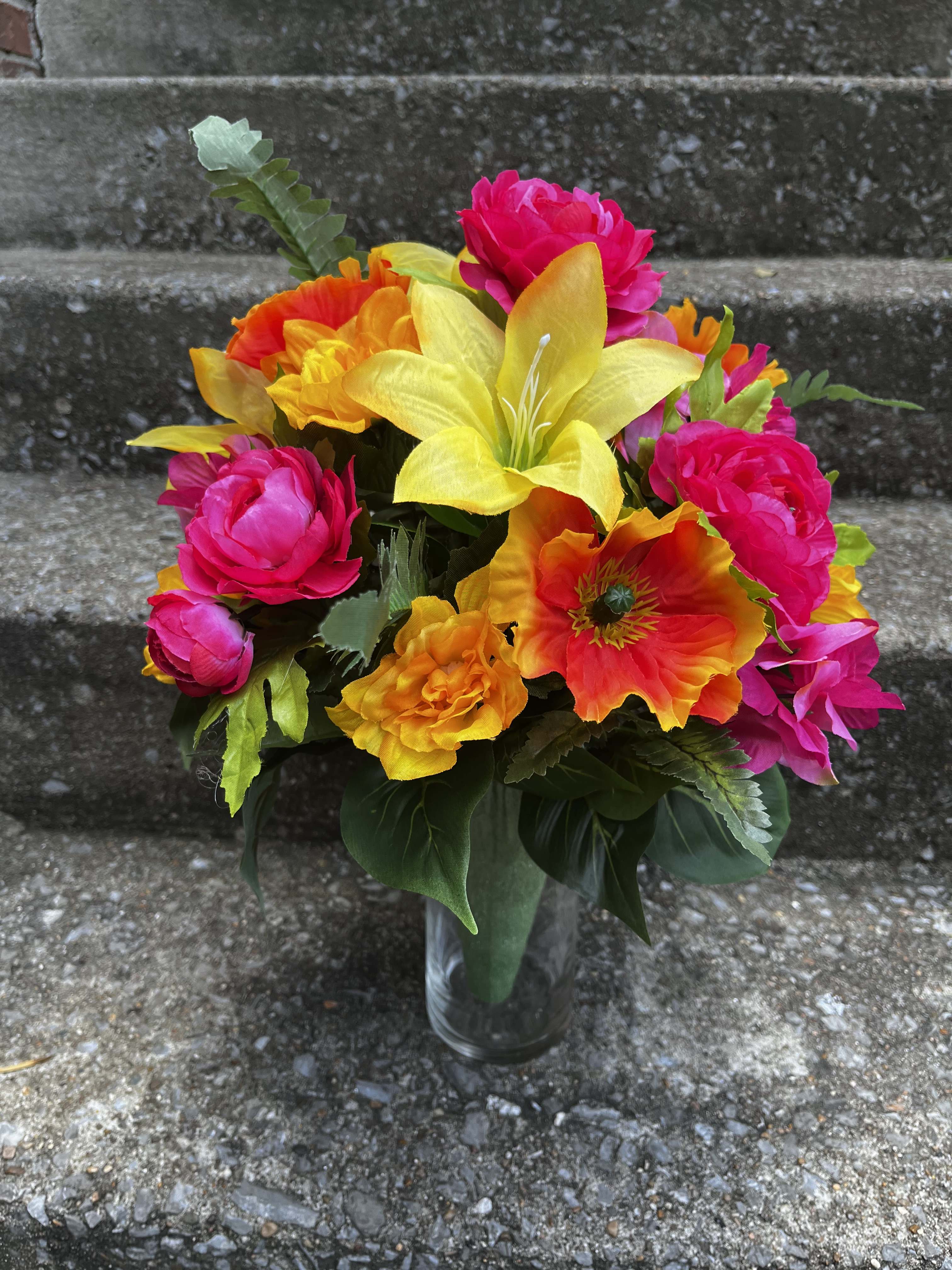 Bright mixed bouquet in a clear glass vase with pink, yellow, and orange blooms.