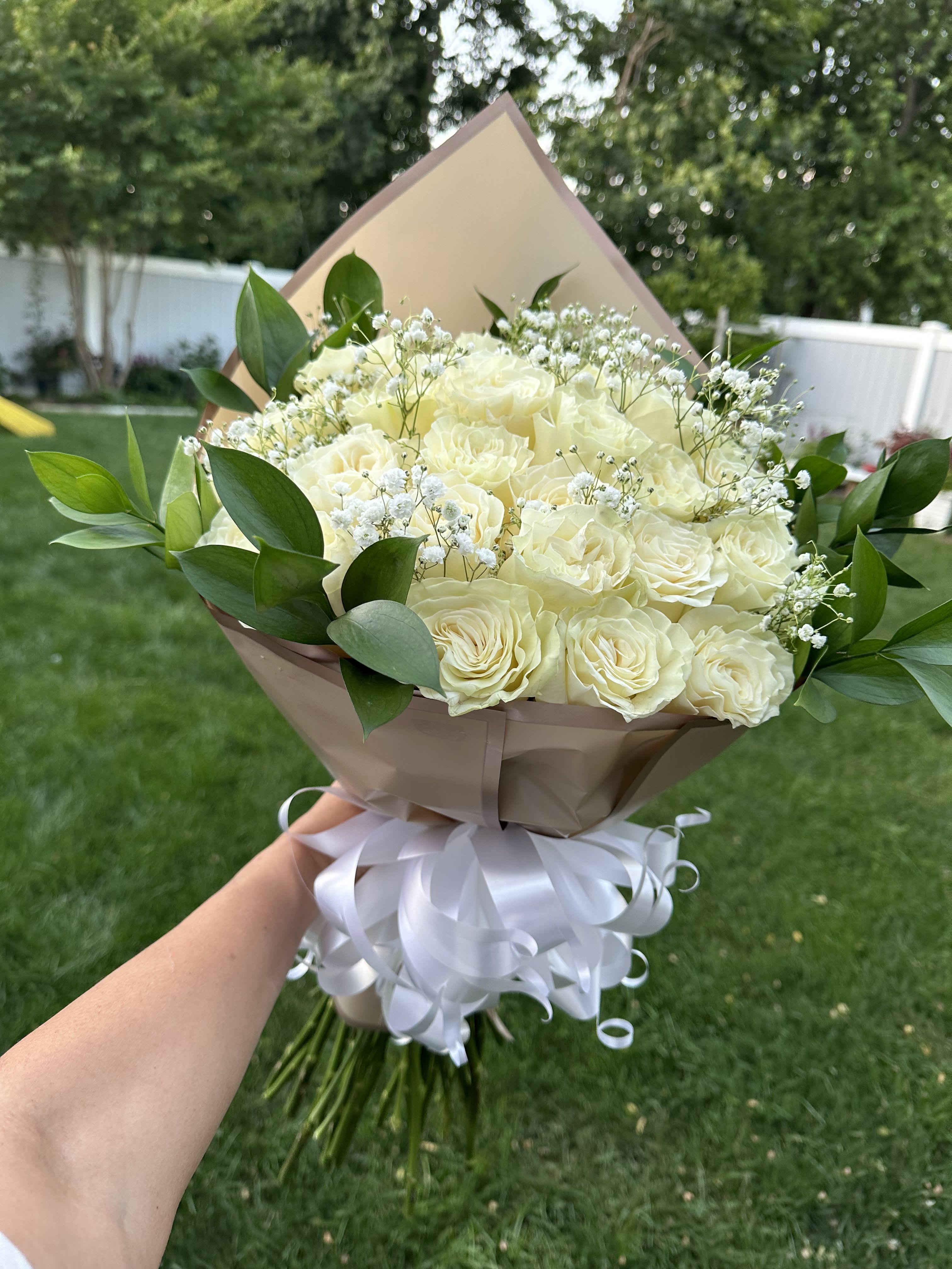 Bouquet of cream roses with baby's breath and greenery, wrapped in tan paper with a white ribbon