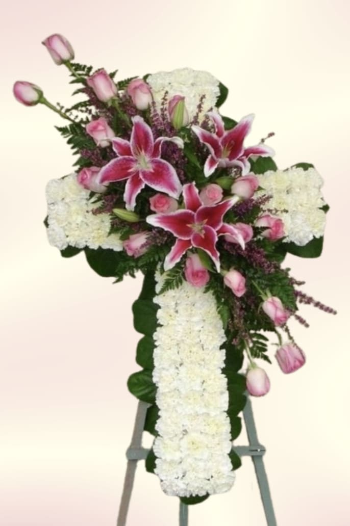 Pink Lily Mini Cross - A tall standing sympathy spray that reads as a graceful tribute, the Pink Lily Mini Cross arranges pink lilies, white roses, and soft carnations into a vertical memorial display perfect for a funeral or graveside service. The easel presentation and cascading white floral panel give this arrangement a ceremonial, reverent silhouette-an elegant way to honor a loved one and offer comfort at a difficult time.  Bright magenta-pink lilies and roses crown the top of the cross, their vivid color drawing the eye against a panel of crisp white blooms and gentle green foliage for contrast and texture. The mix of lilies, roses, and carnations creates layered shapes and a soft scent profile while maintaining a formal, high-contrast palette of pink, white, and green.  Designed to stand beside a casket or mark a graveside, this arrangement communicates sympathy and respect-she'll feel remembered and honored by the thoughtful floral gesture. Arrives mounted on an easel for immediate display; handle with care when transporting and place in cool, sheltered conditions until service time.