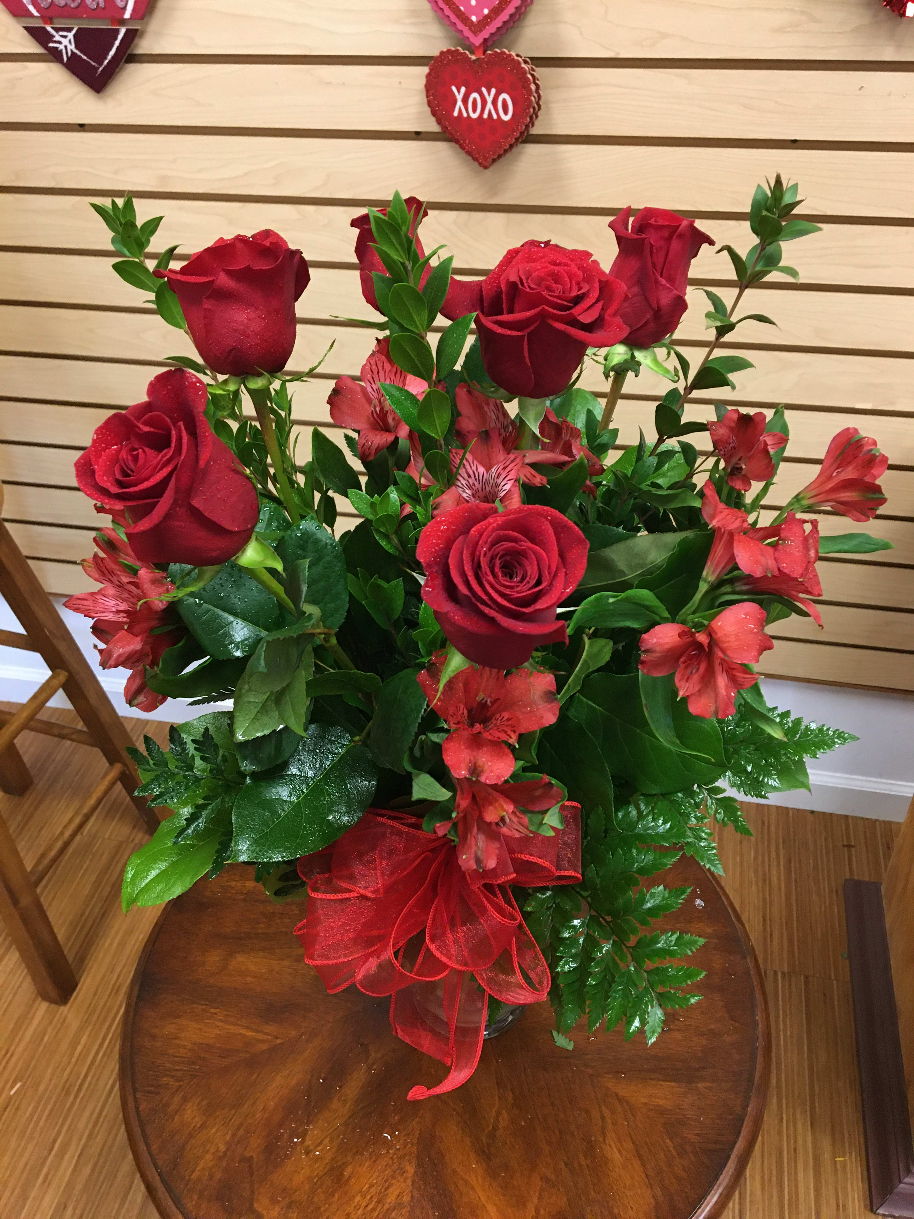 Red roses and red alstroemeria in a glass vase with a red ribbon