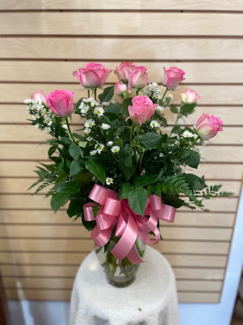 Pink roses arranged in a clear glass vase with a pink ribbon bow