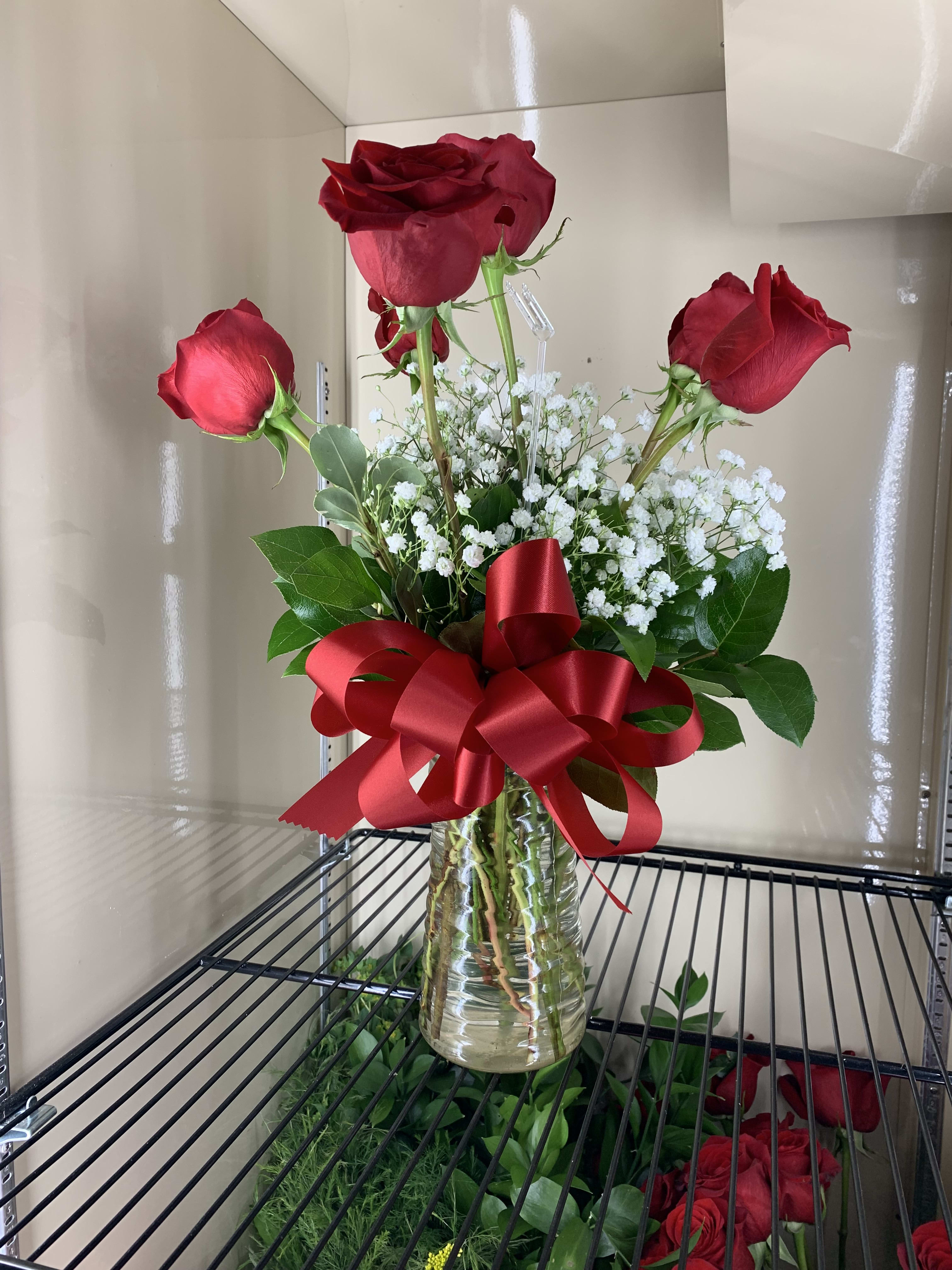 Three red roses in a glass vase with white baby's breath and a red ribbon