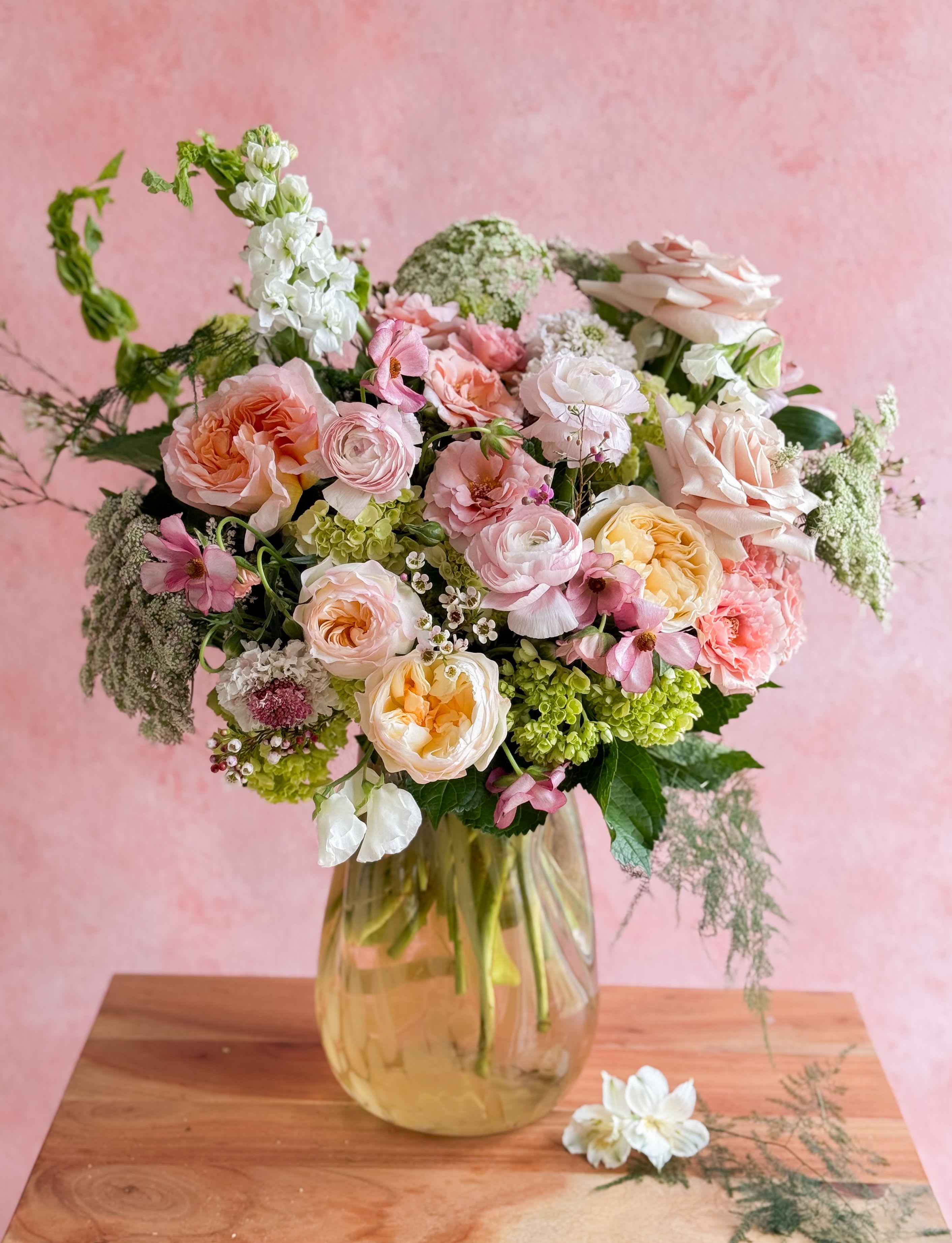 Pastel bouquet of roses, ranunculus, and mixed blooms in a glass vase
