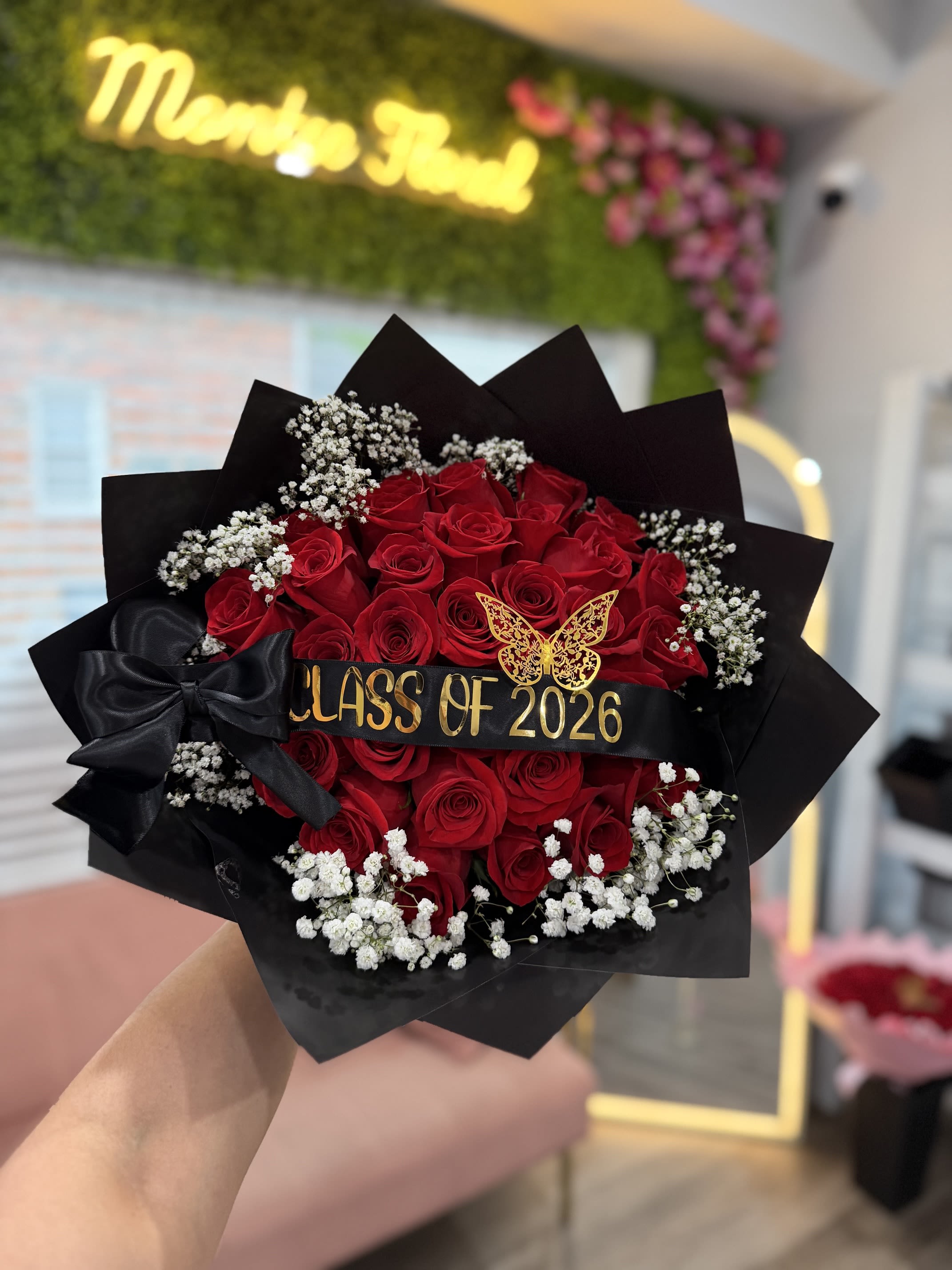 Class of 2026  - Tightly packed  red roses with white baby's breath, wrapped in black paper with satin bow, goldcustom banner and butterfly pick
