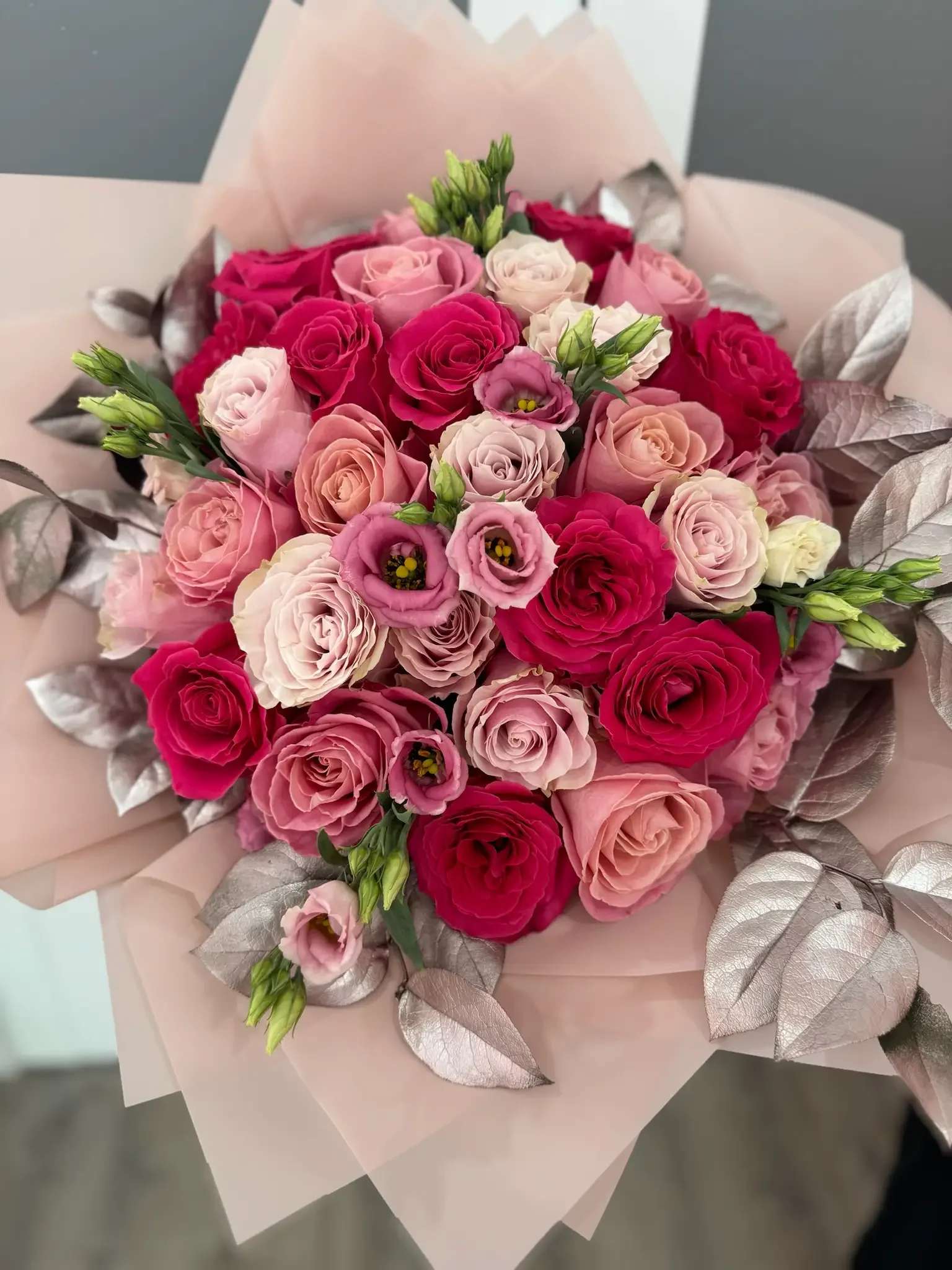 Bouquet of pink and red roses with pale wrapping and metallic leaves