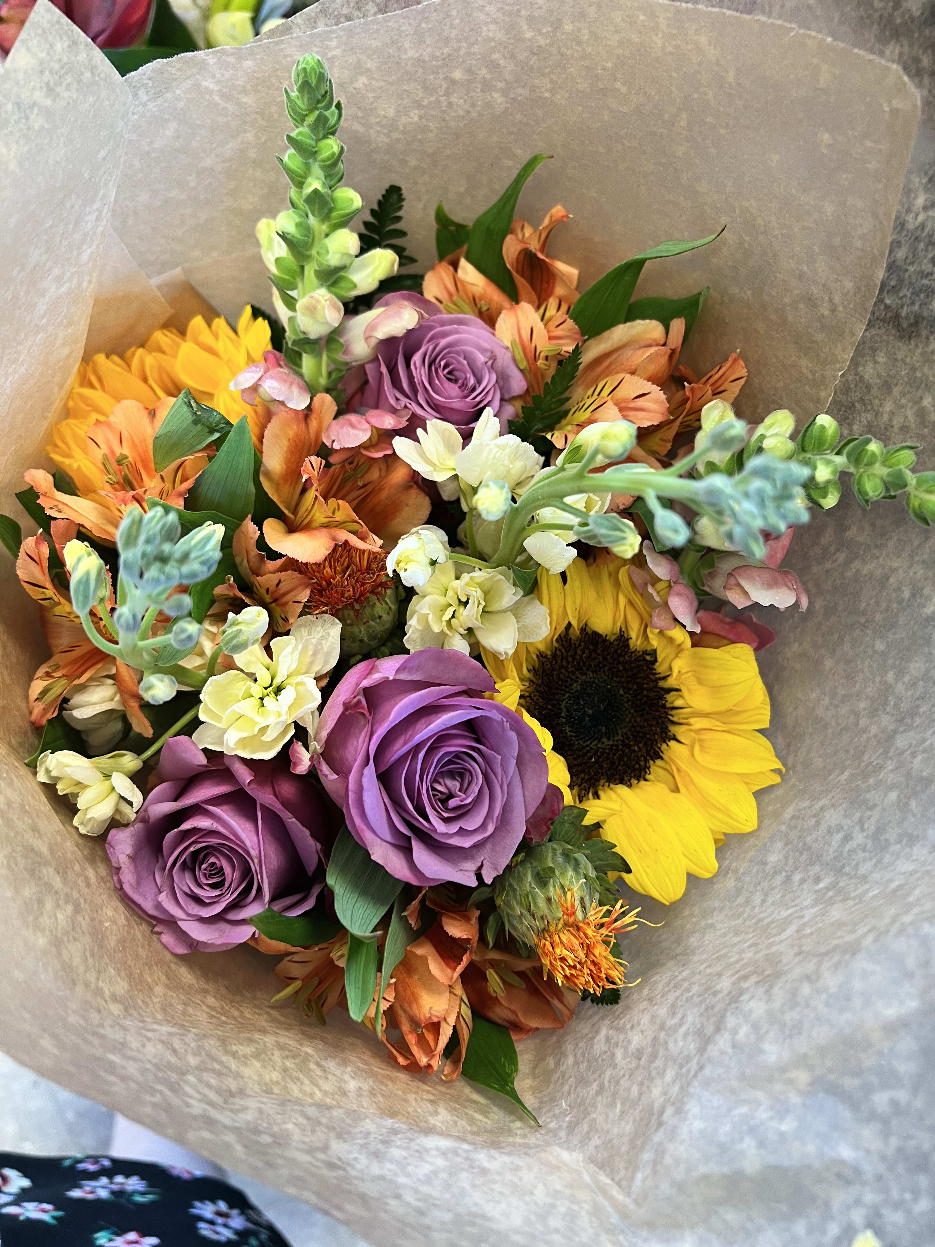 Bouquet of purple roses, sunflowers, and orange mixed blooms wrapped in paper