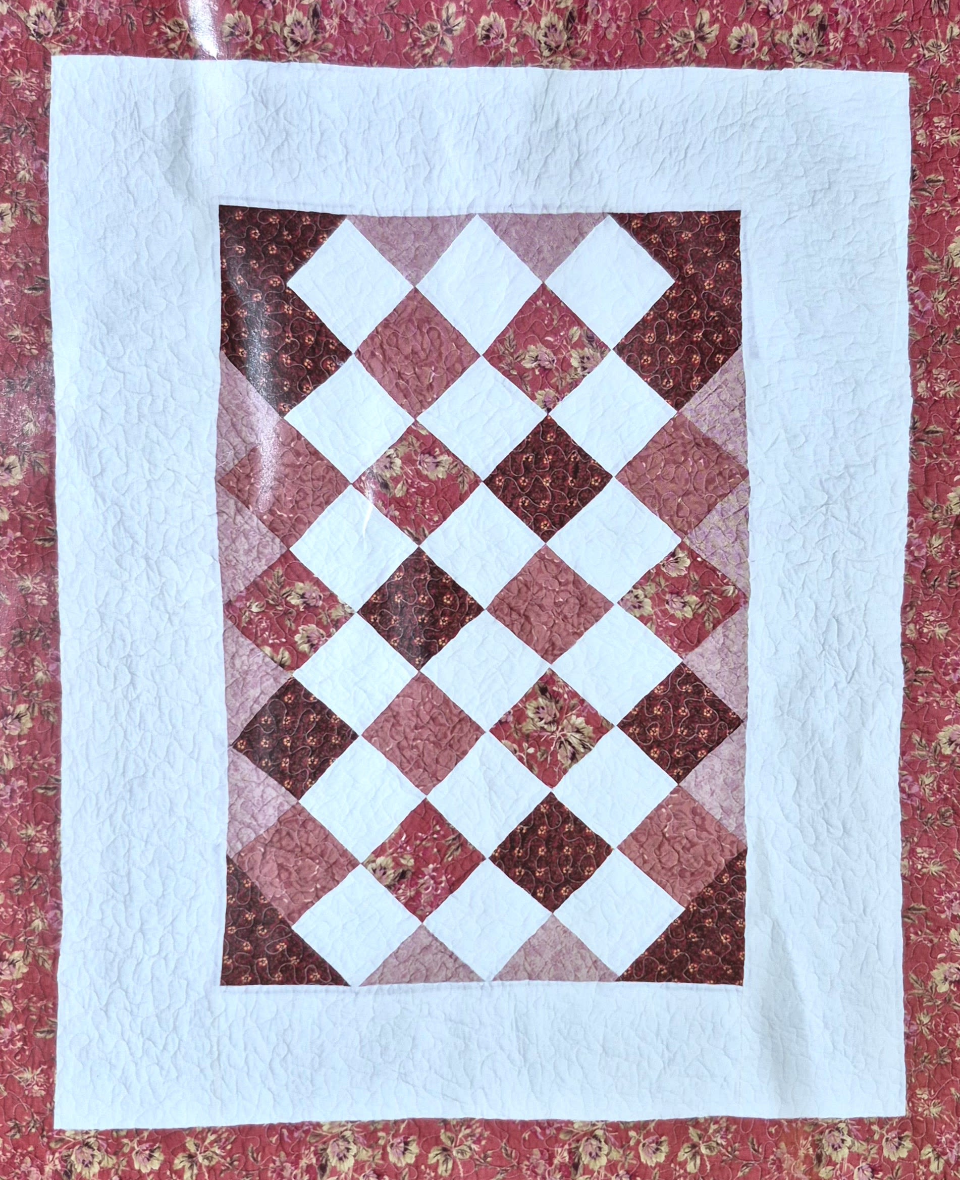 Patchwork quilt with a diamond pattern in pink, red, and white