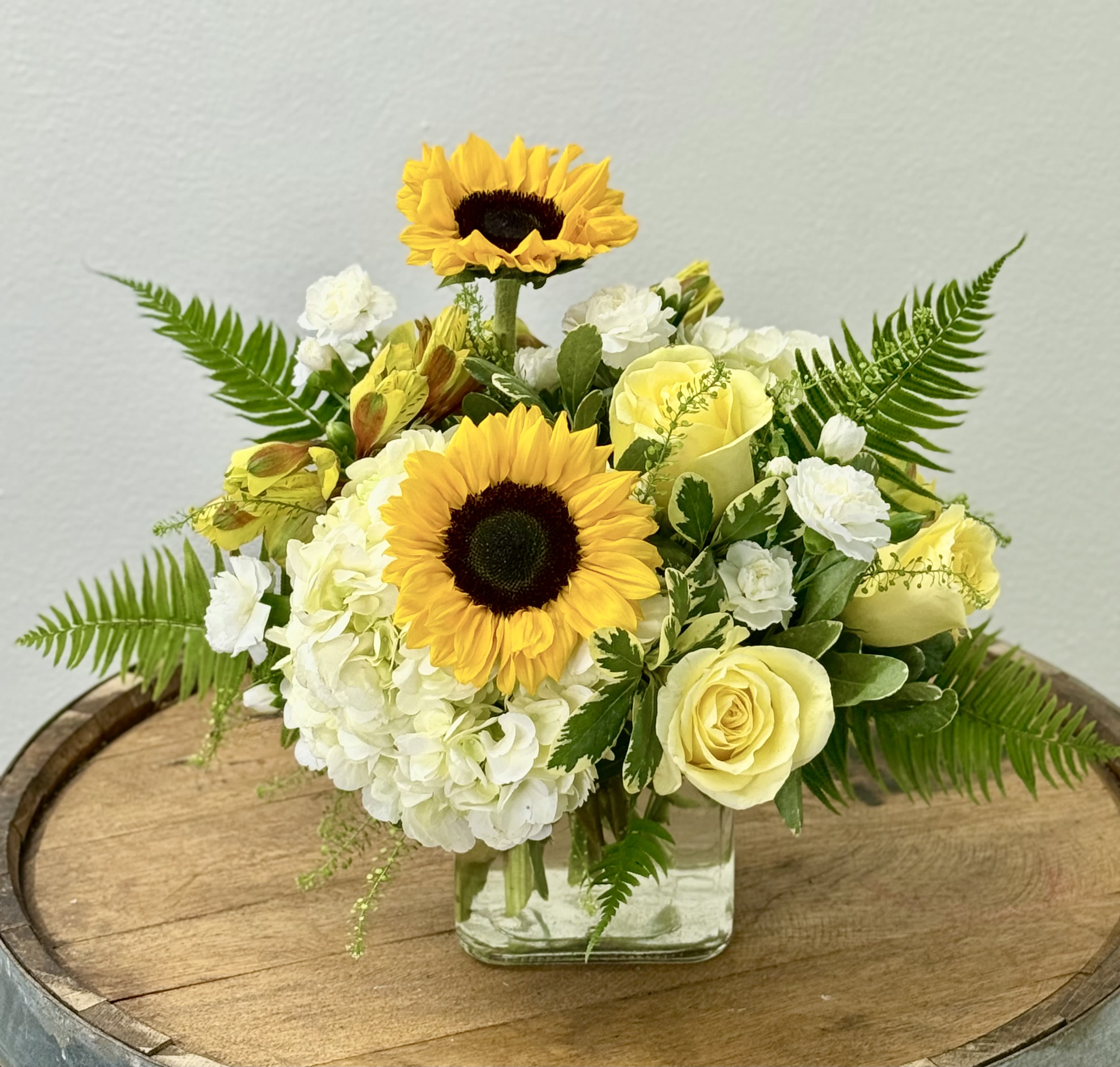 Yellow sunflowers and pale roses in a clear square vase