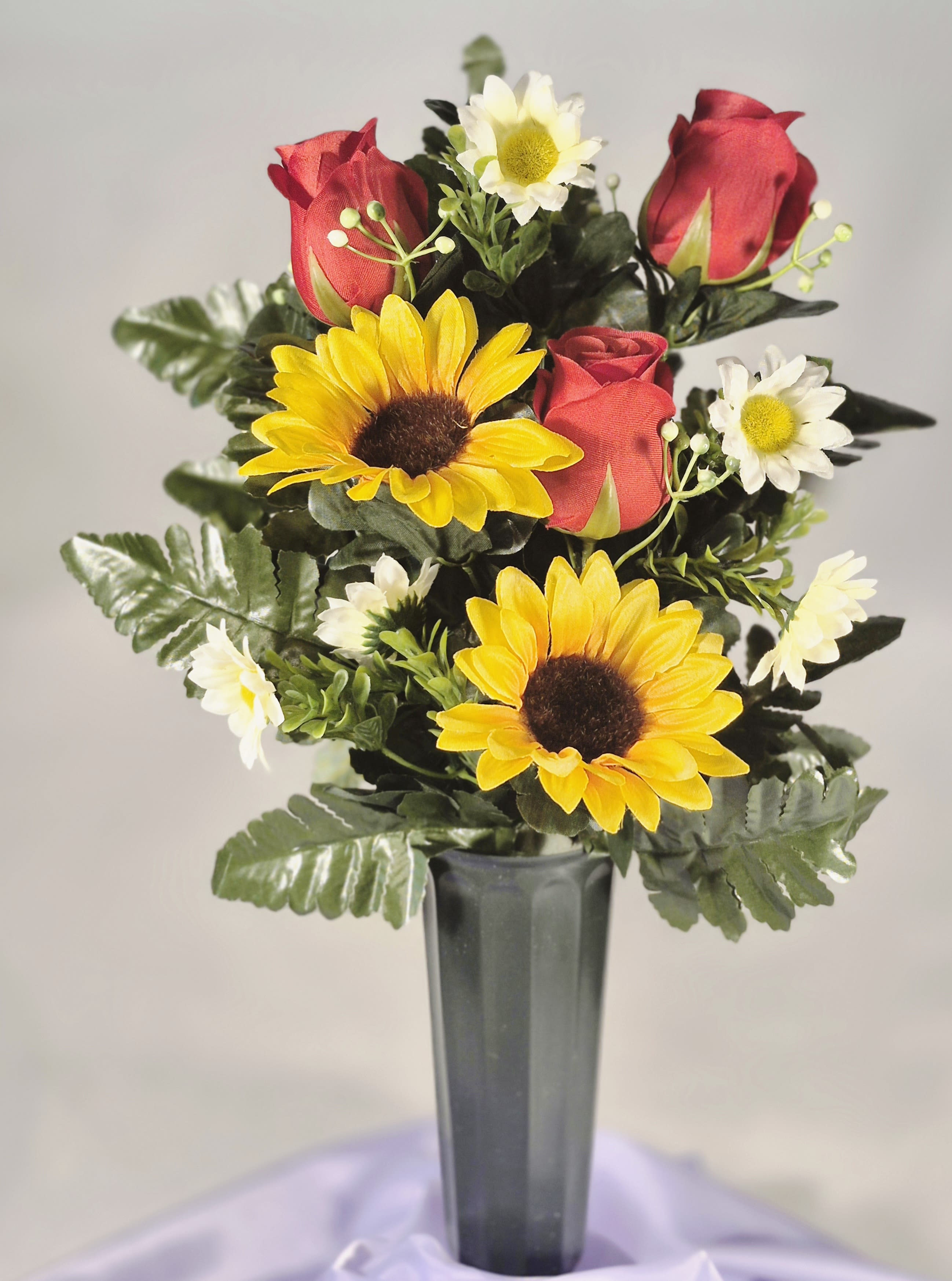 Cemetery Silk Rose &amp; Sunflower Bouquet - Bright yellow sunflower blooms paired with deep red rose buds create a striking cemetery flower arrangement for memorials, birthdays, or a thoughtful thank-you display. This cemetery silk rose &amp; sunflower bouquet presents a cheerful, lively contrast of red and yellow with small white daisy accents and glossy green foliage, giving the person you're honoring a warm, uplifting presence at their resting place.  The bouquet is arranged compactly and upright in a tall green 2" vase, with artificial silk roses, sunflowers, and fern-like greenery secured in a foam-filled plastic base for stability. At approximately 16" tall, the memorial cone offers a neat, formal silhouette that holds its color and shape season after season without watering or maintenance.