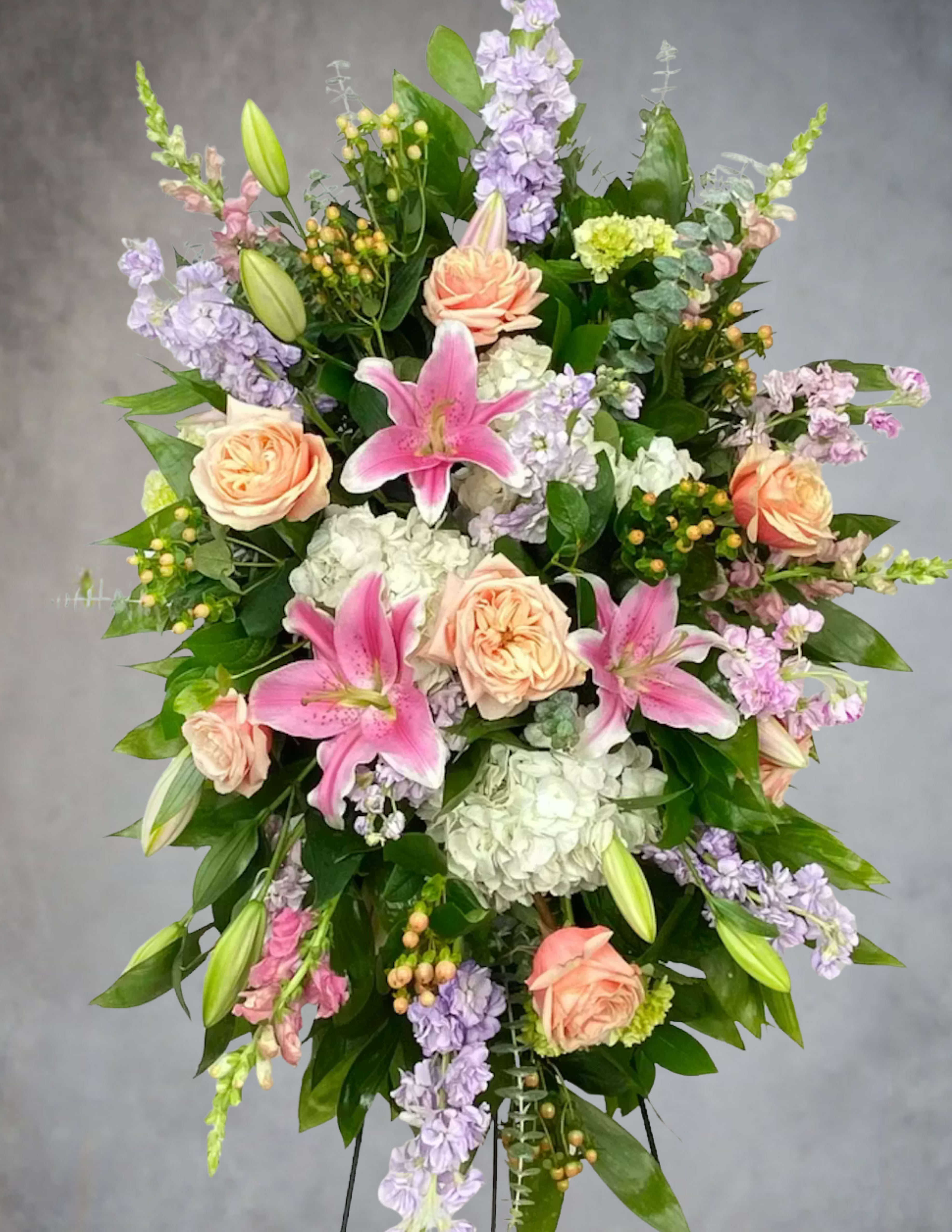 Standing floral spray with pink lilies, peach roses, and lavender blooms