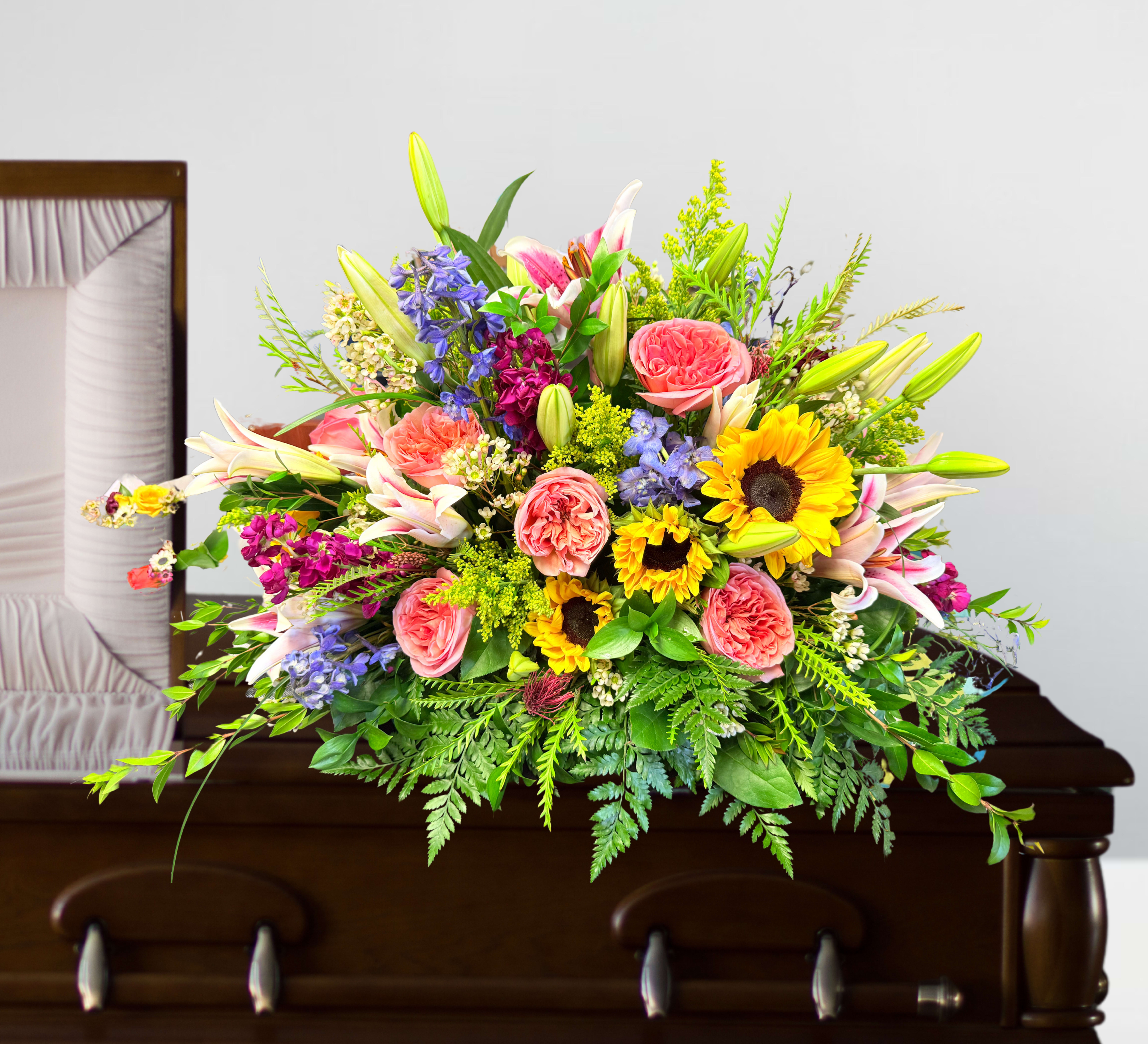 Sincerely loved casket spray - Sincerely Loved Casket Spray  Honor a life sincerely loved with this breathtaking Sincerely Loved Casket Spray, a vibrant and heartfelt tribute. This stunning arrangement is beautifully designed with graceful Stargazer lilies, delicate pink Expression roses, and radiant sunflowers, symbolizing love, warmth, and remembrance. Accented with elegant delphinium and lush stock, this spray brings a touch of softness and serenity, creating a meaningful farewell.  Rich in color and sentiment, this casket spray serves as a loving expression of admiration and deep respect. A fitting tribute for a beautiful soul, it offers comfort and beauty to those mourning while celebrating a life well-lived and cherished.