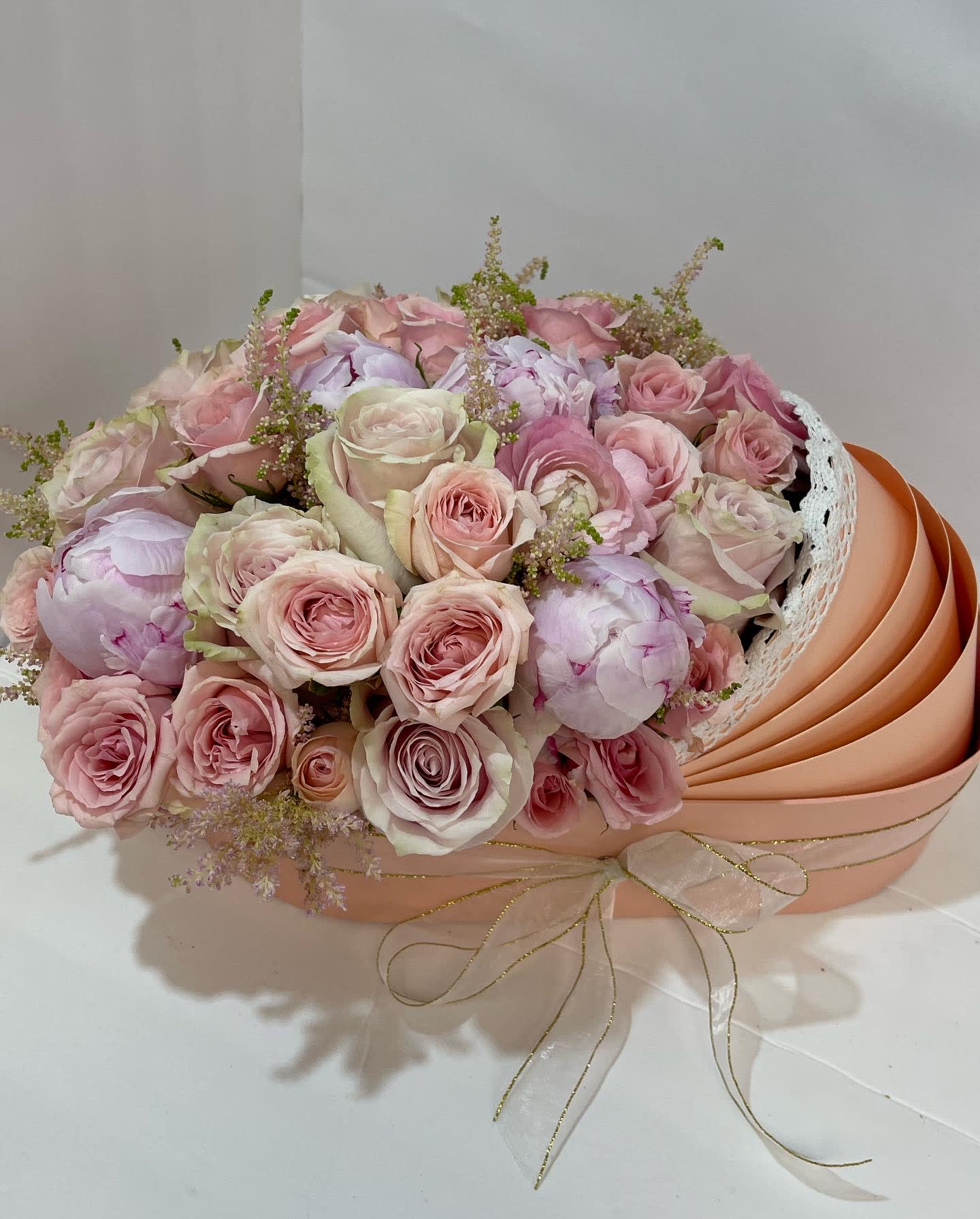 Bouquet of pale pink roses and peonies in a peach hatbox