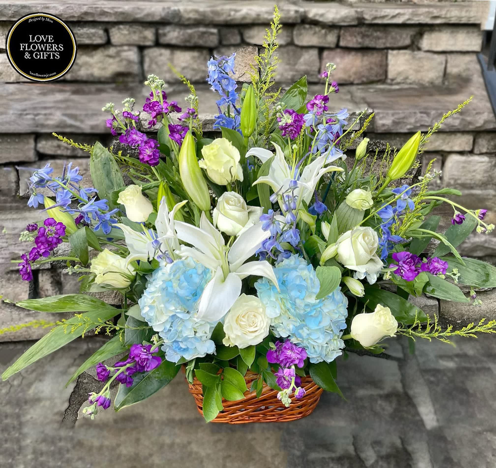 Basket arrangement of white lilies and roses with blue hydrangeas and purple blooms