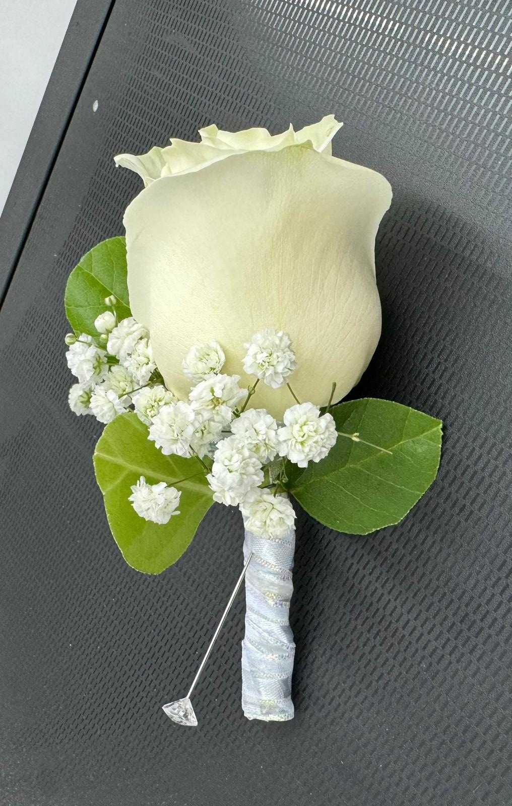 White rose boutonniere with baby's breath and green leaves