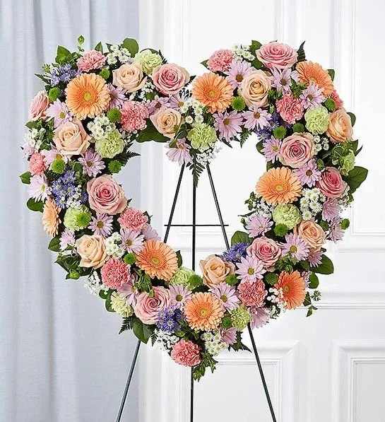 Heart-shaped floral wreath on a stand with pink, peach, and lavender blooms