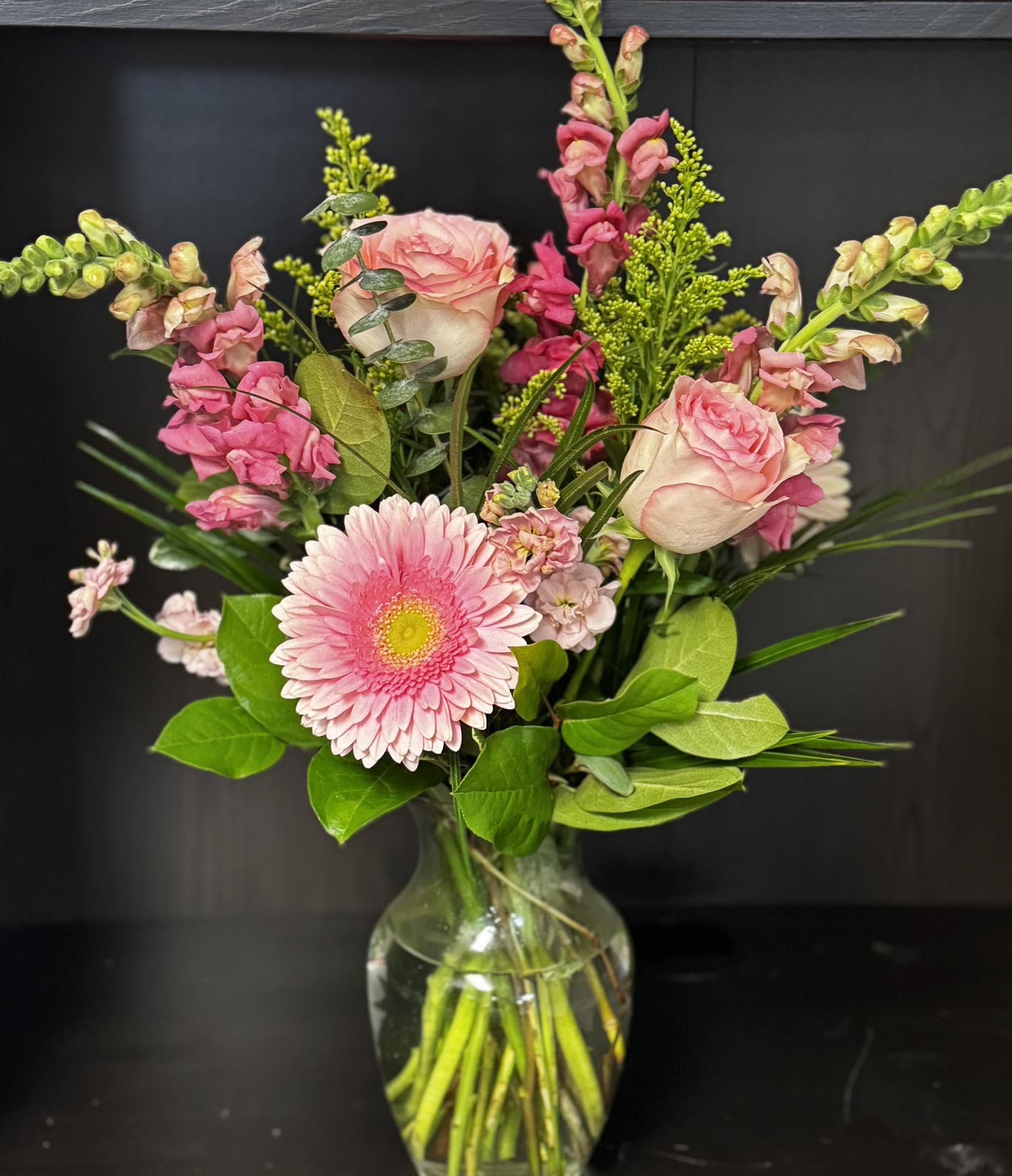 pretty in pink - A cheerful, romantic bouquet built around soft pinks and fresh greenery, perfect as a birthday bouquet, thank-you arrangement, or everyday gift to show appreciation.   This mixed-color display pairs blush and magenta blooms with bright green filler and broad foliage for a garden-style texture. Stems are presented in a simple clear glass vase so the natural lines remain visible and the focus stays on the flowers' color and form. The palette of pink, white and green gives this arrangement versatile appeal for friends, colleagues, moms, or anyone who will feel noticed and loved.  Sized to sit easily on a table or desk, the arrangement is designed for immediate impact and simple care: keep fresh water in the vase and trim stems if you notice shortening blooms. It's an easy, elegant way to make someone feel truly celebrated.