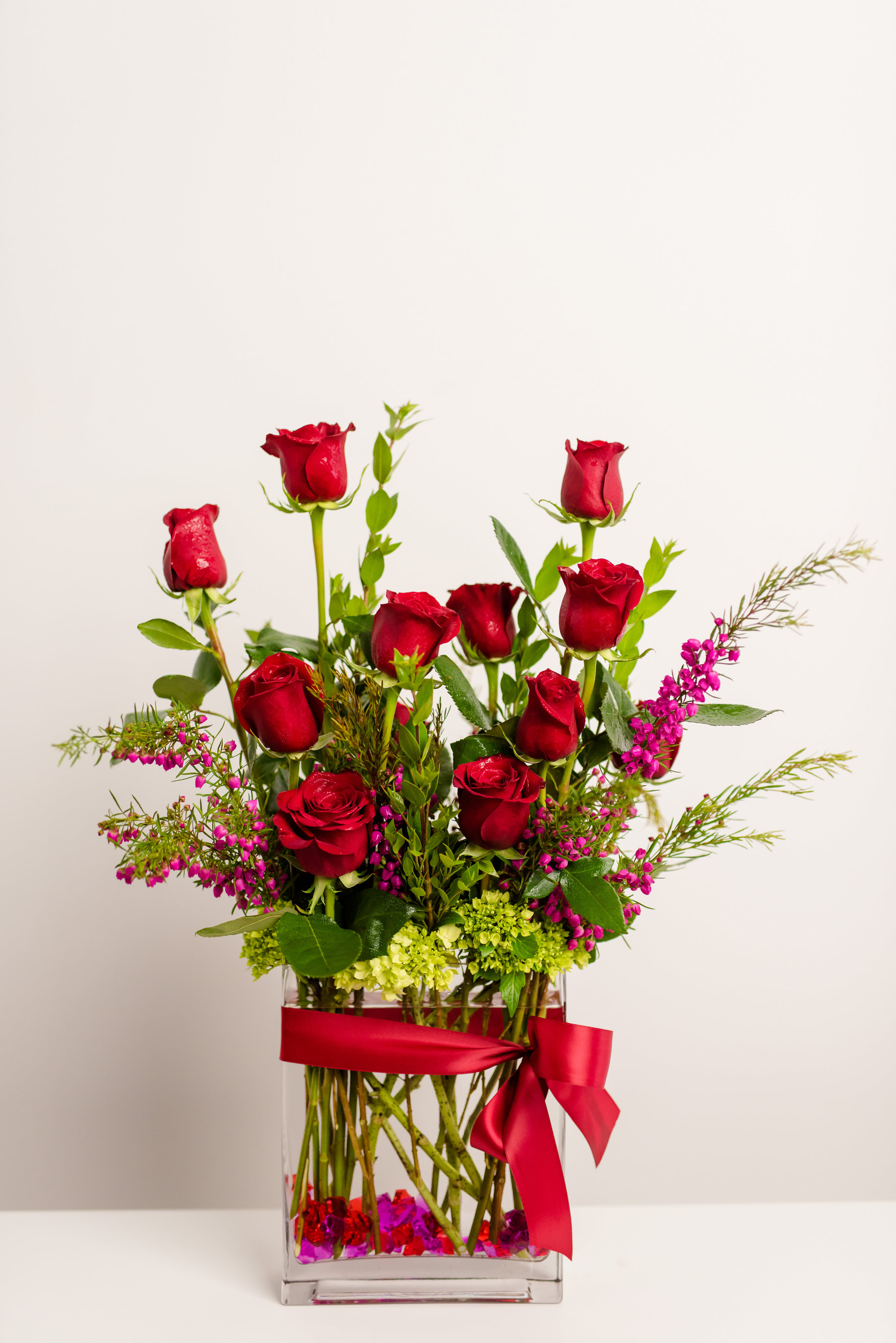 Red roses in a clear square vase with a red ribbon