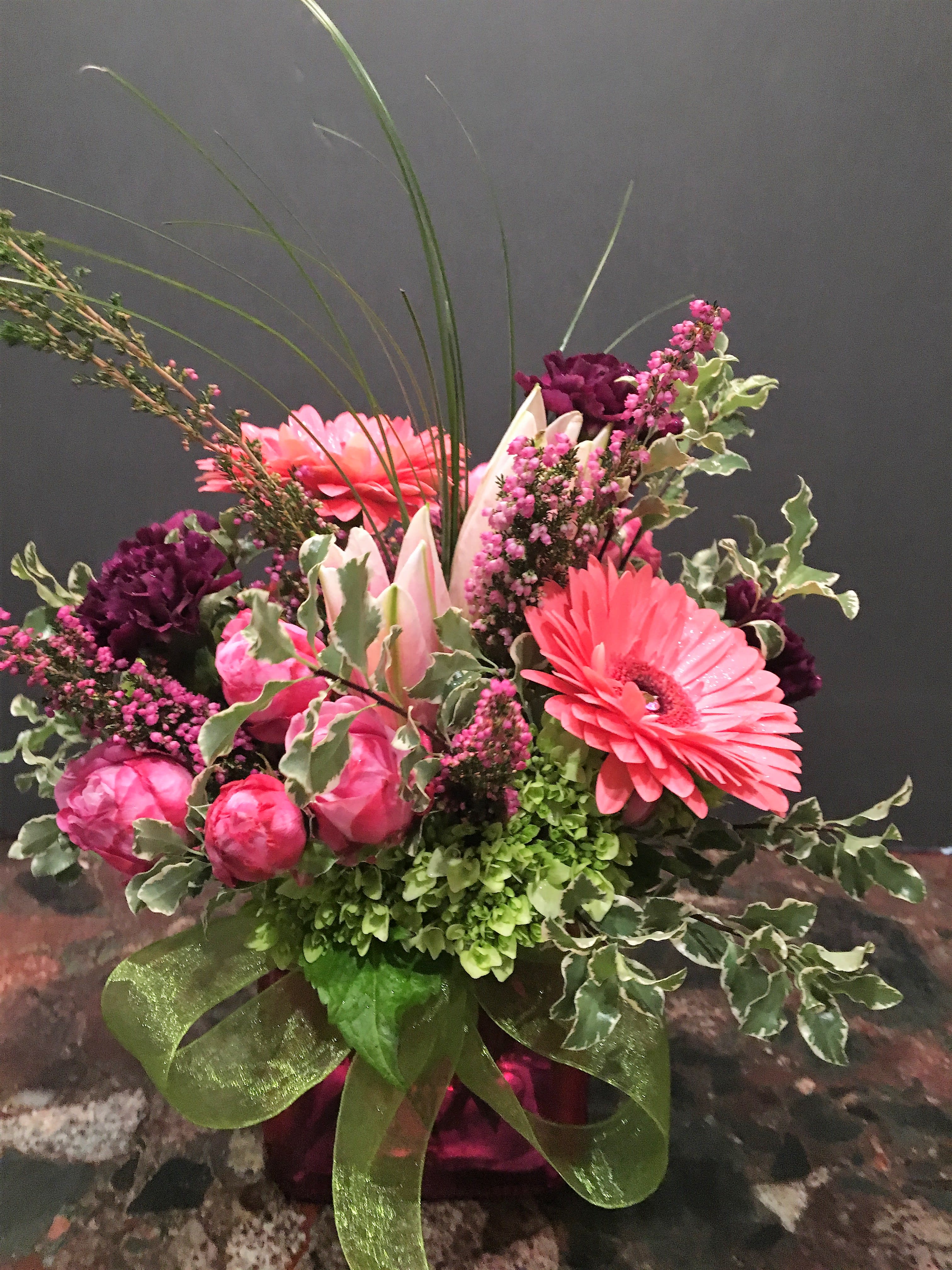 Pink and purple floral arrangement in a glass vase with a green ribbon