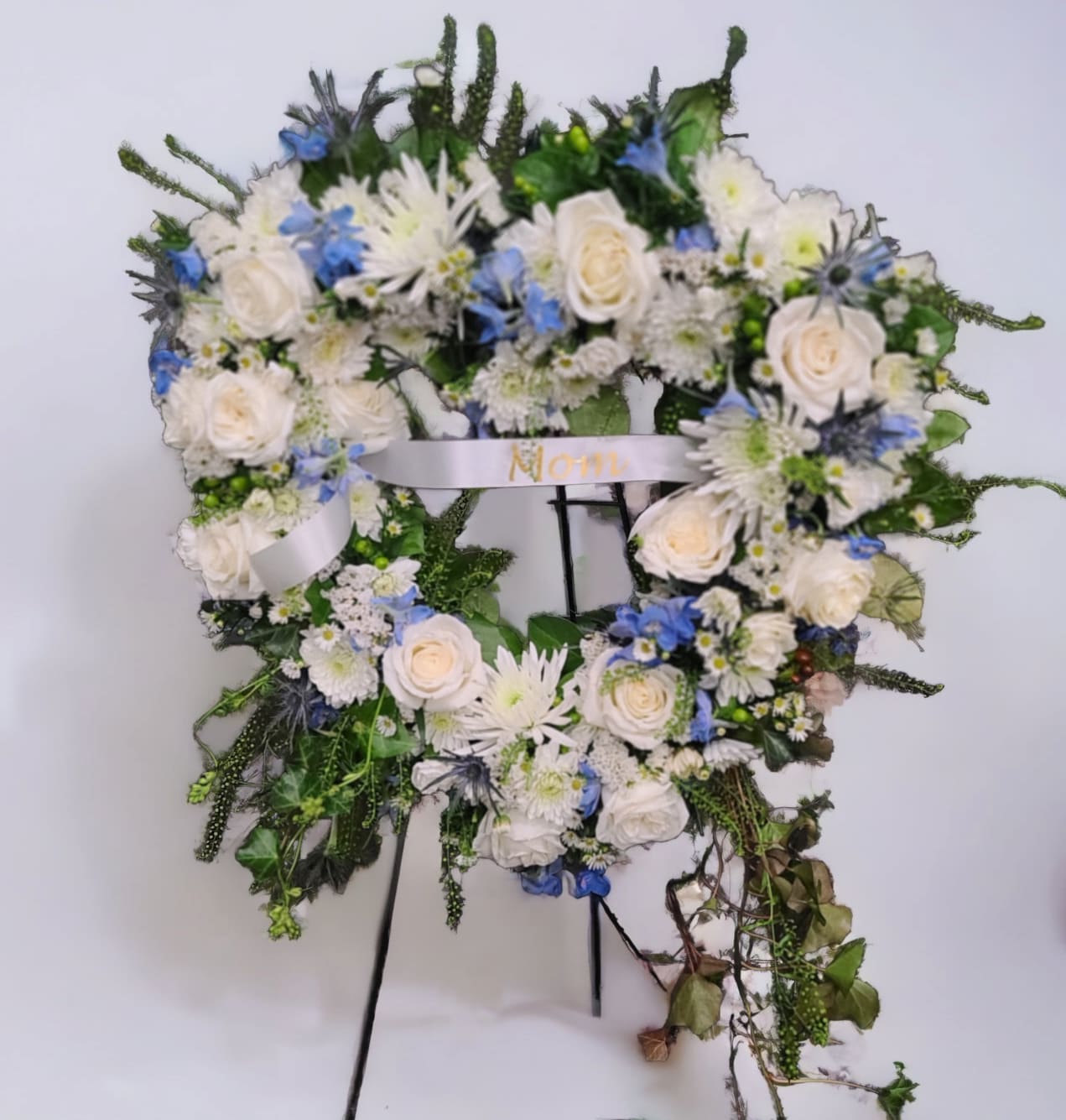 Heart-shaped floral wreath with white roses and blue flowers on a stand