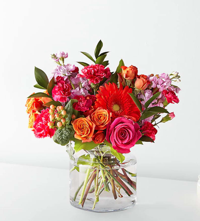 Bright mixed bouquet of roses, gerbera daisies, and carnations in a clear glass vase