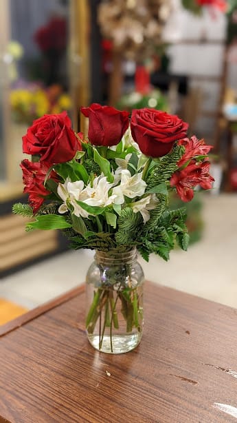 Red roses and white flowers arranged in a glass jar vase