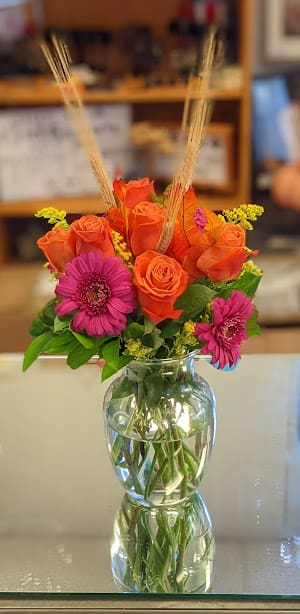 Orange roses and pink gerbera daisies in a clear glass vase