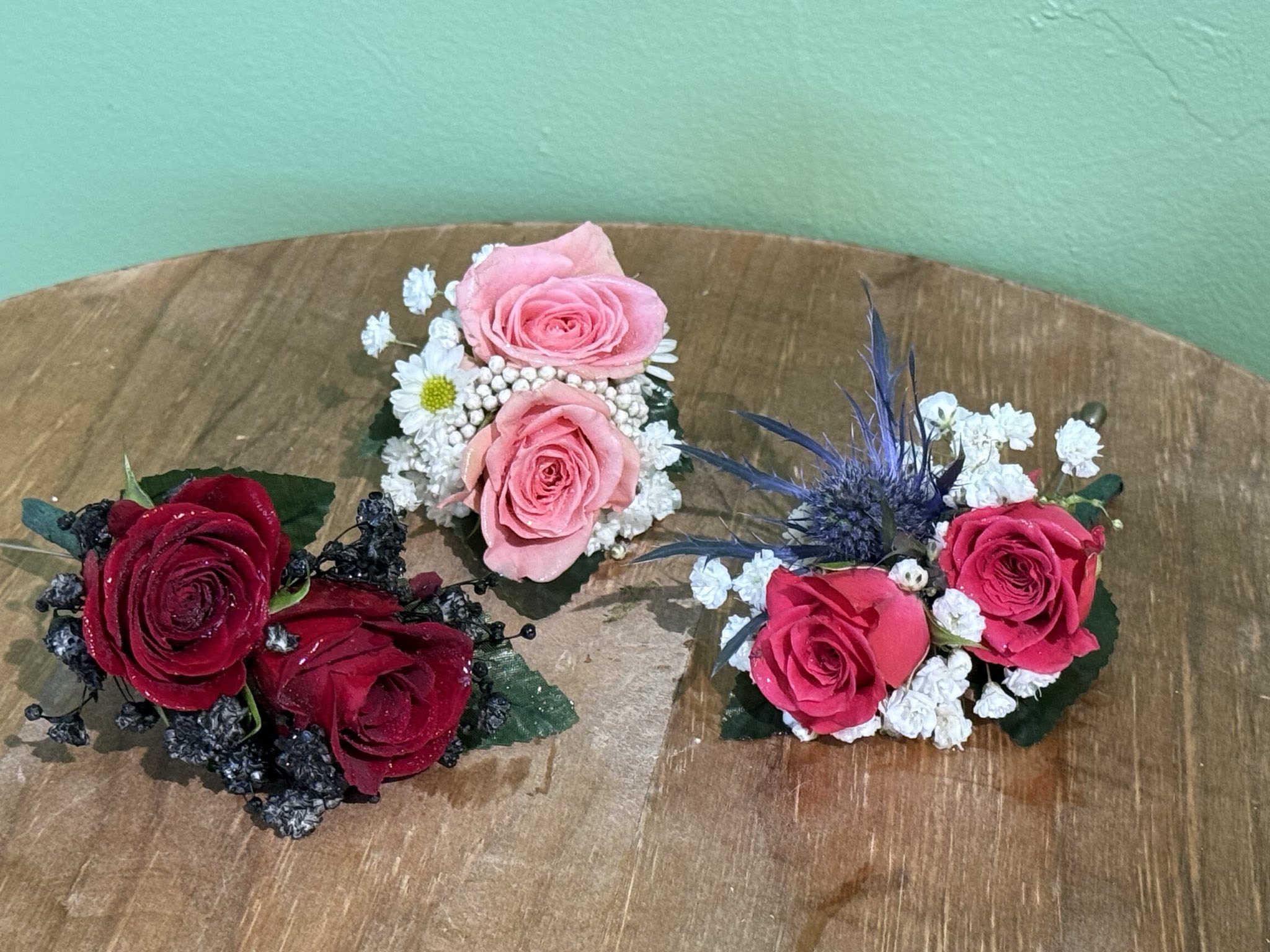 Three small rose corsages with baby's breath on a wooden surface