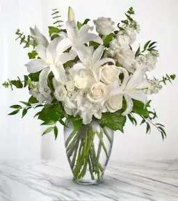 White lilies and roses arranged in a clear glass vase