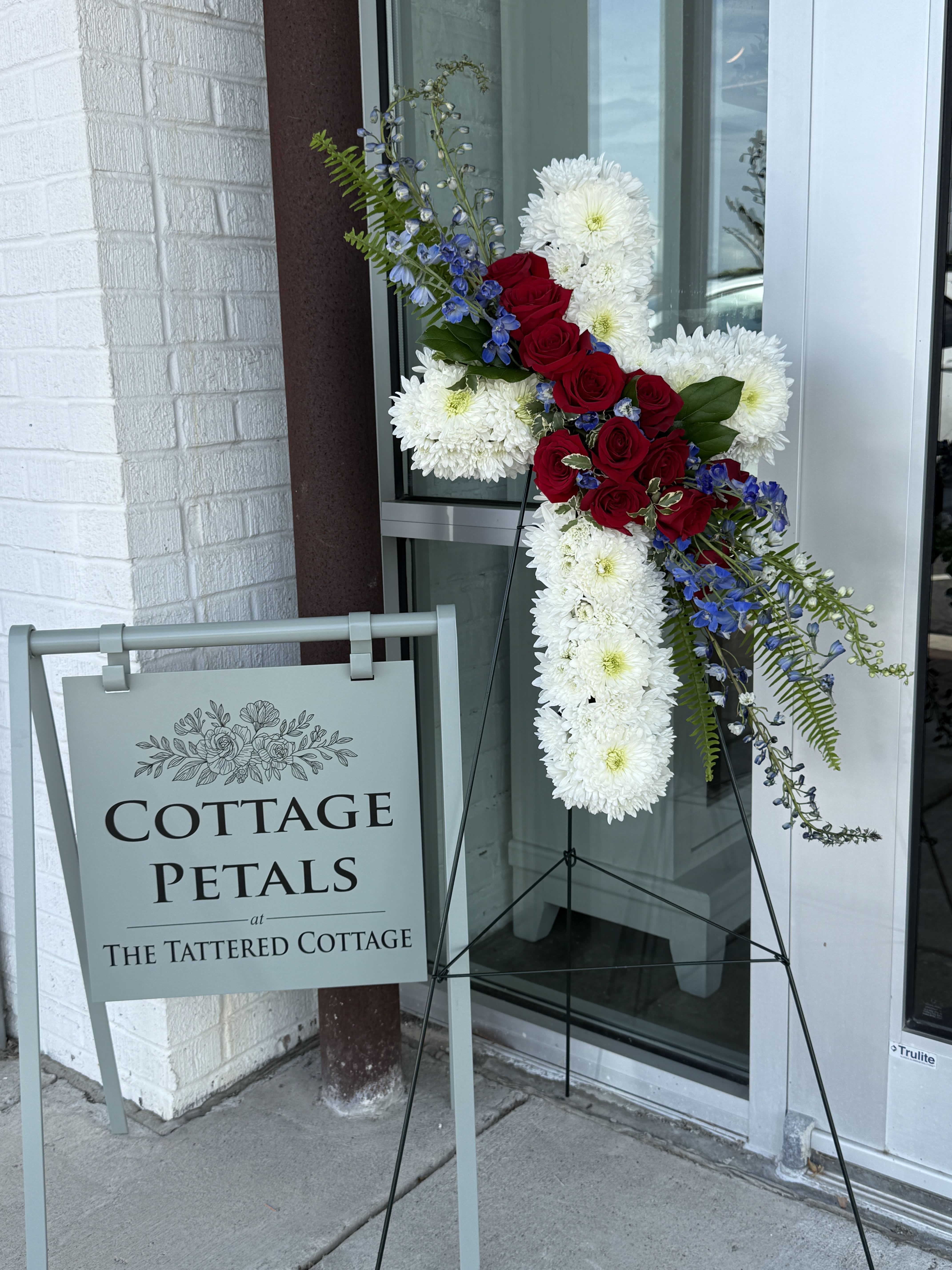 Honor &amp; Faith Cross - A striking tribute of love, sacrifice, and remembrance, the Honor &amp; Faith Cross features rich red roses nestled among soft white chrysanthemums and elegant greenery, creating a timeless and meaningful display. Designed in the shape of a cross, this standing arrangement symbolizes peace, devotion, and everlasting love while offering comfort during times of loss.  Its bold red and white color palette makes it especially fitting for honoring veterans, first responders, or loved ones remembered for their strength, courage, and unwavering spirit.  Flower varieties and greenery may vary slightly based on seasonal availability, but the overall style, fullness, and color palette will always be maintained.