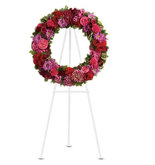 Circular floral wreath on a white easel with pink and red flowers