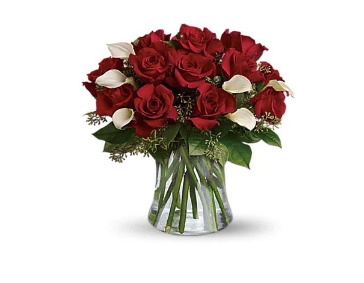 Red roses with white calla lilies in a clear glass vase