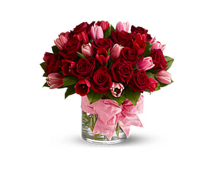 Bouquet of red roses and pink tulips in a glass vase with a pink ribbon