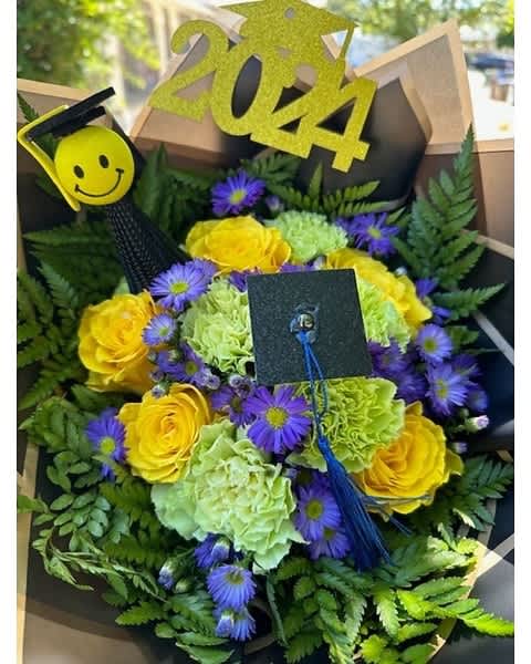 Graduation bouquet with yellow roses, green carnations, purple asters and grad-themed picks reading 2024.