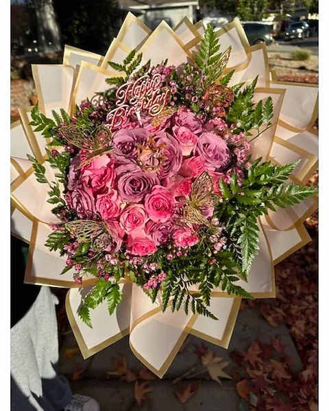 Large round bouquet of pink and lavender roses with birthday pick and butterflies in cream wrap