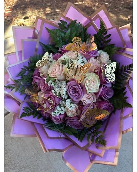Hand-tied bouquet of lavender and cream roses with white filler flowers, wrapped in lilac paper with gold butterflies.