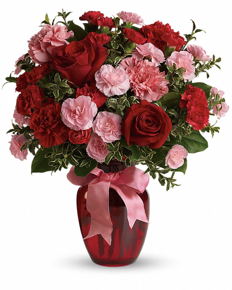 Red and pink carnations and roses in a red glass vase with a pink ribbon