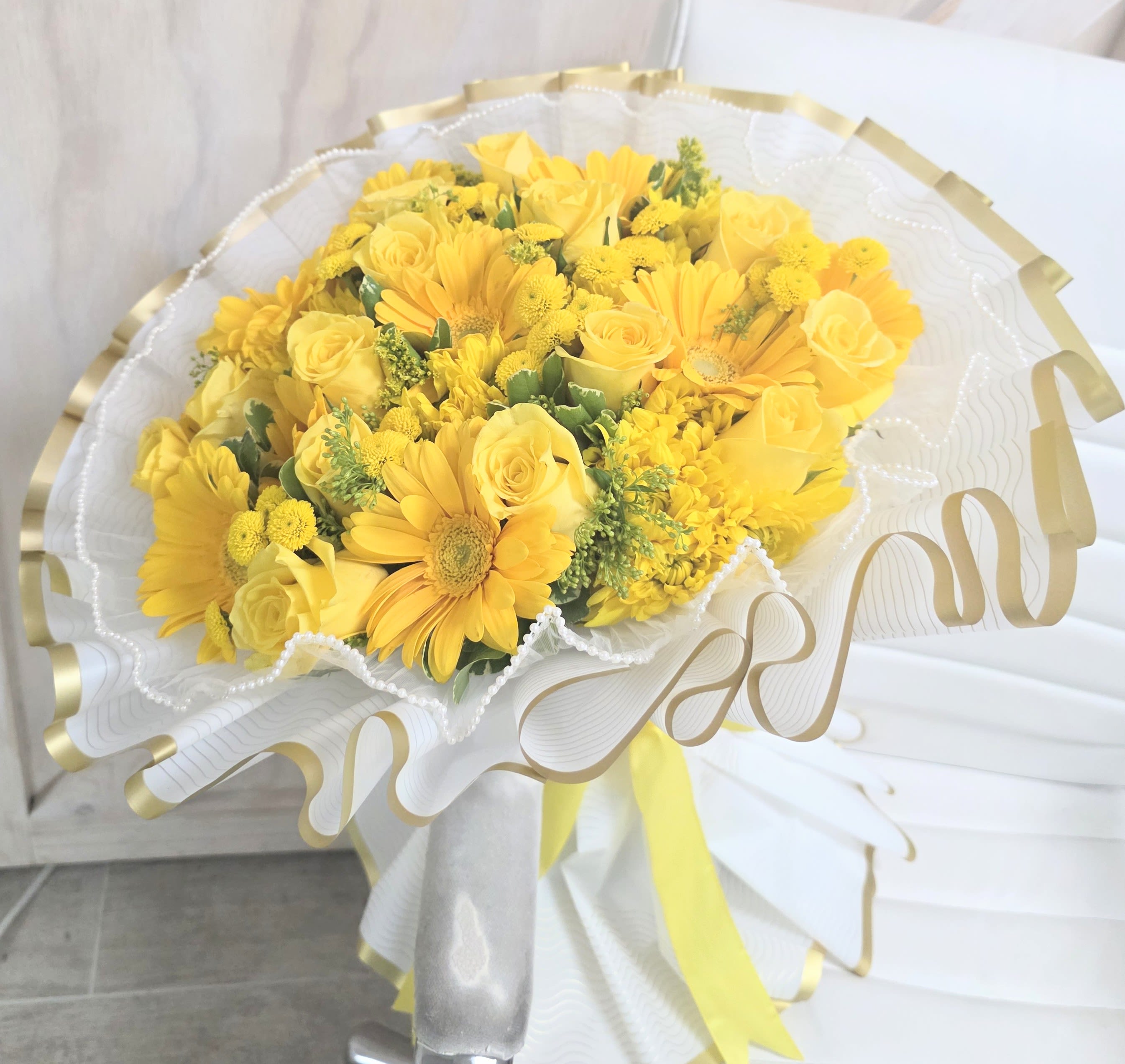 Premium Yellow Ramo - Premium wrapped bouquet with pearl sheer trim and a mix of yellow roses, Gerber daisies, chrysanthemum,  button, daisy, and pittosporum. This represents, love,  joy, happiness and friendship.