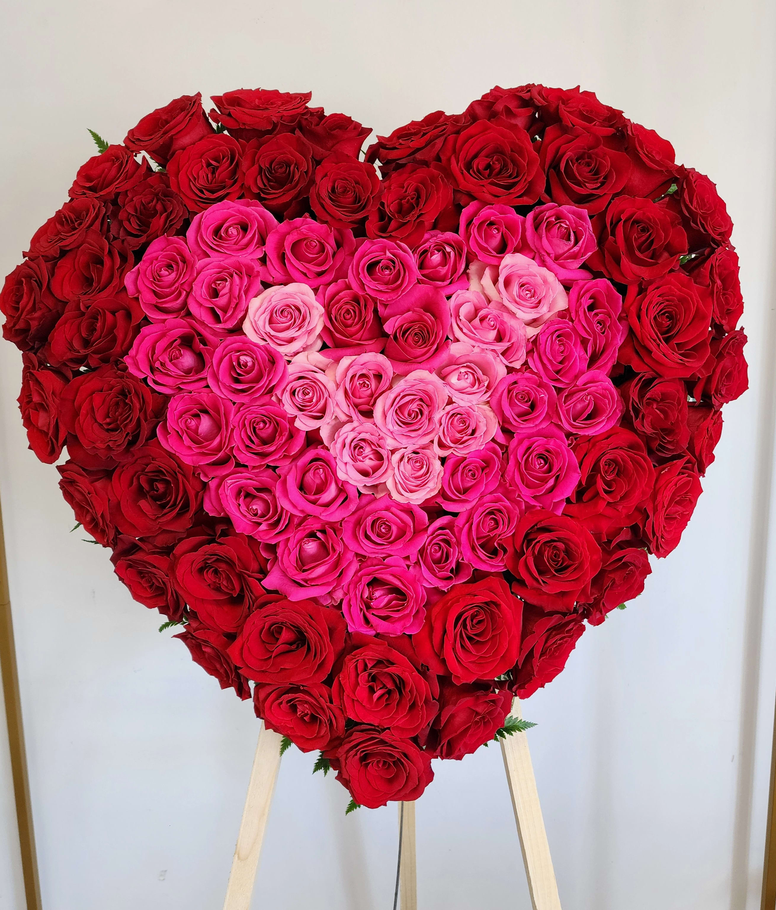 Heart-shaped rose arrangement in red and pink tones on a stand
