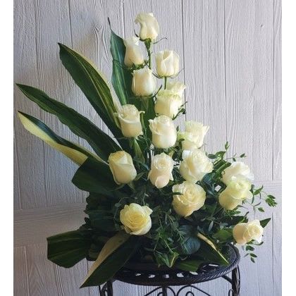 Tall arrangement of white roses with broad dark green leaves